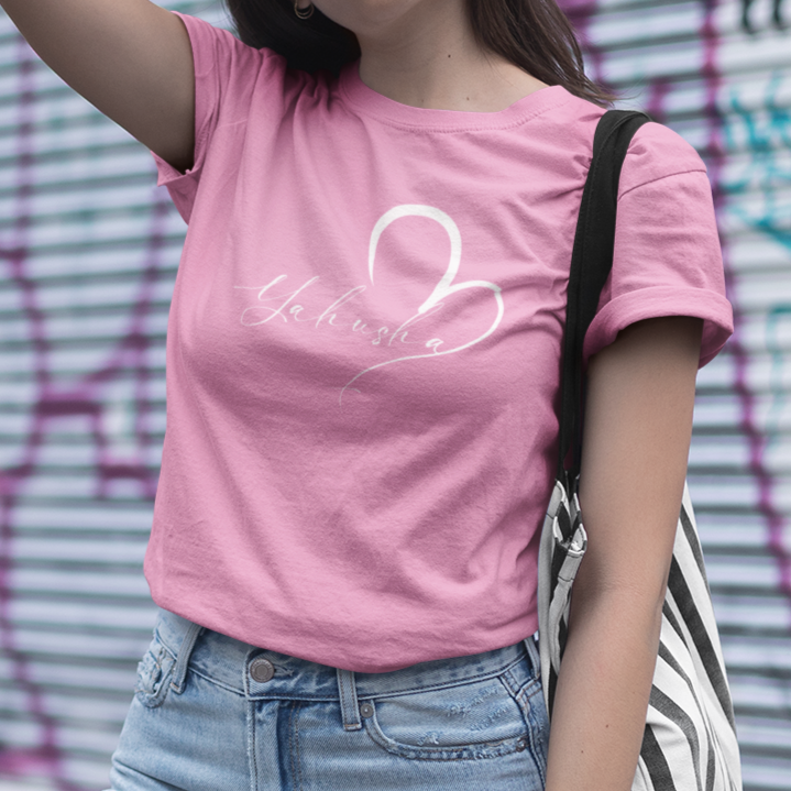 Woman wearing a pink t-shirt with a white logo in front of a graffiti-covered wall.