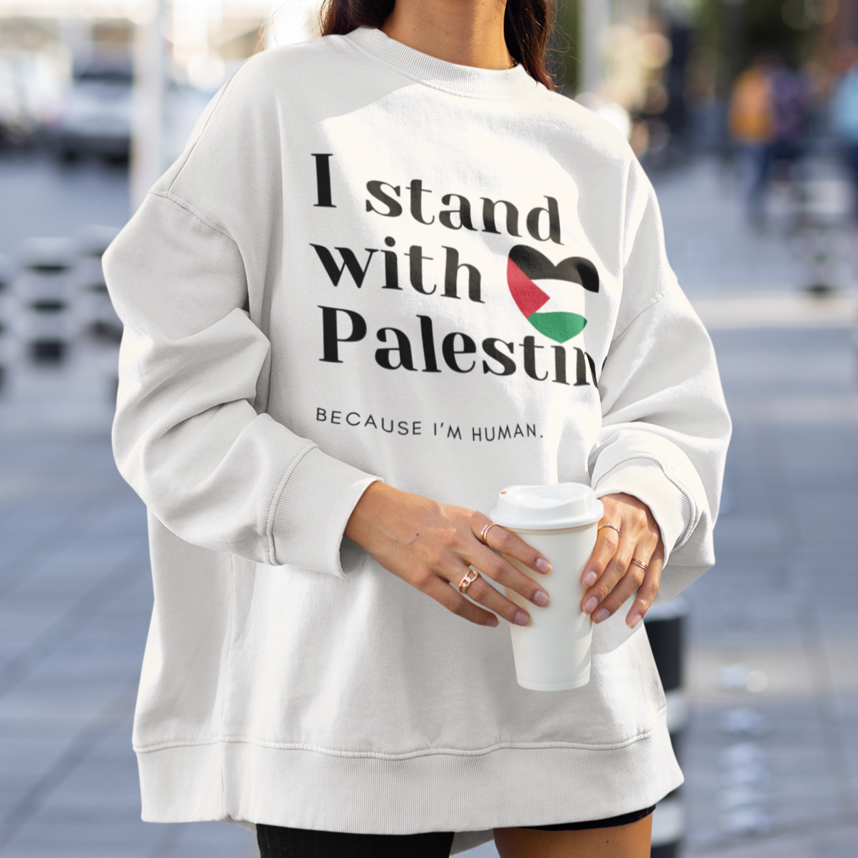 Person wearing a white sweatshirt with 'I stand with Palestine' text on a city street.