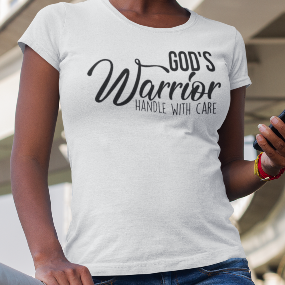 Woman wearing a white t-shirt with 'God's Warrior Handle with Care' text, standing outdoors.