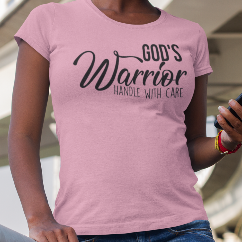 Person wearing a pink t-shirt with 'God's Warrior Handle with Care' text, standing outdoors.