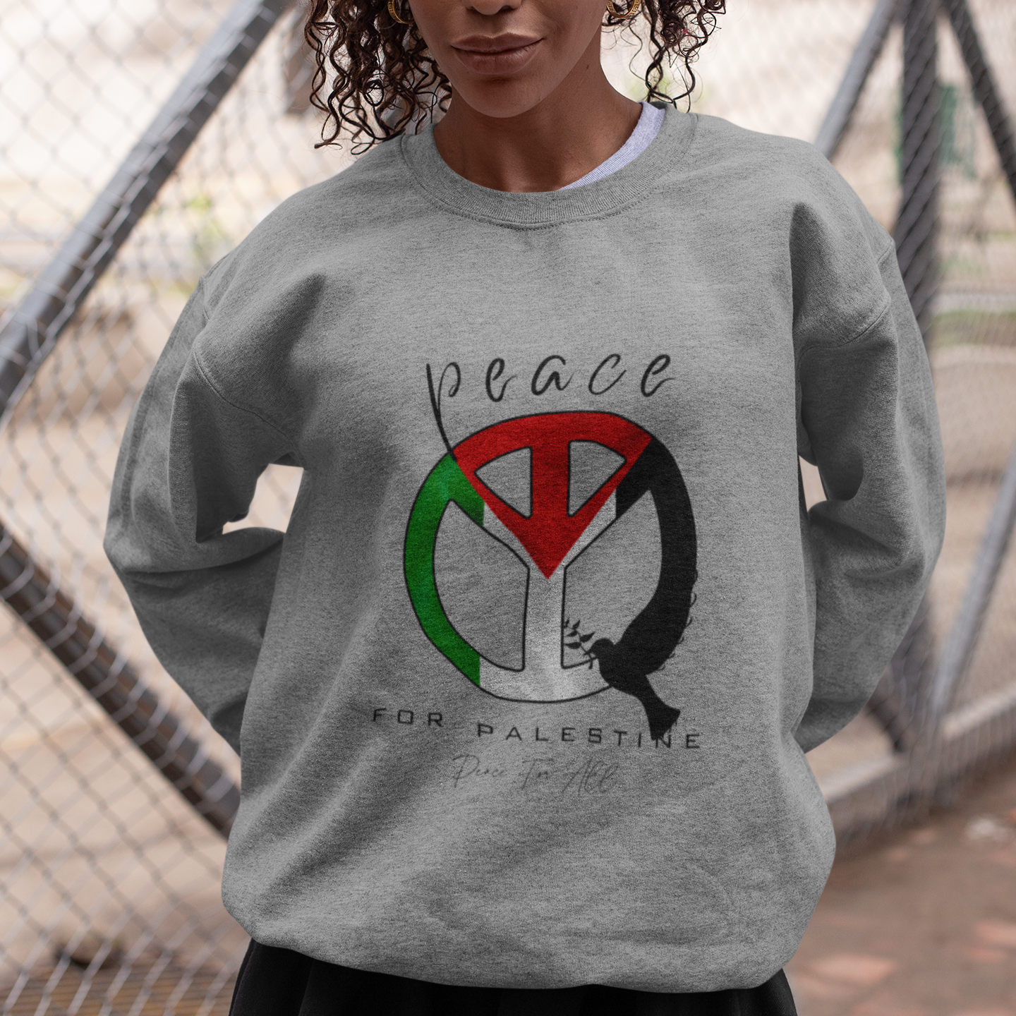 Person wearing a gray sweatshirt with a peace symbol design in front of a chain-link fence.