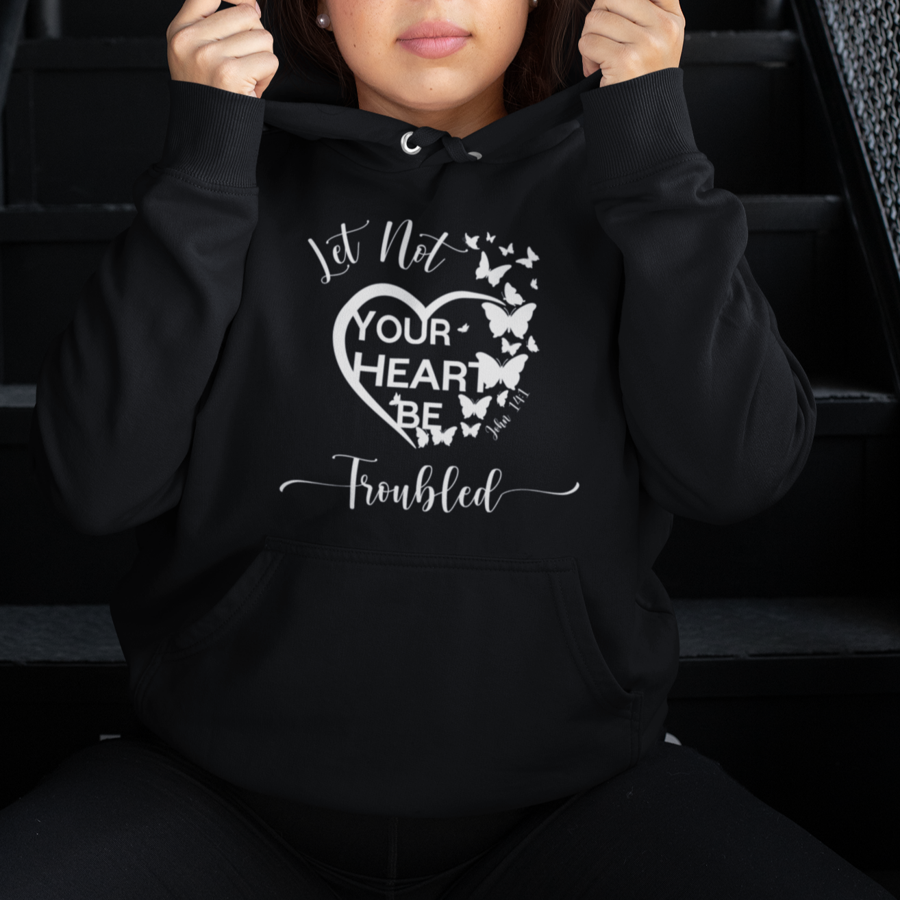 Person wearing a black hoodie with a heart design and text, sitting on stairs.