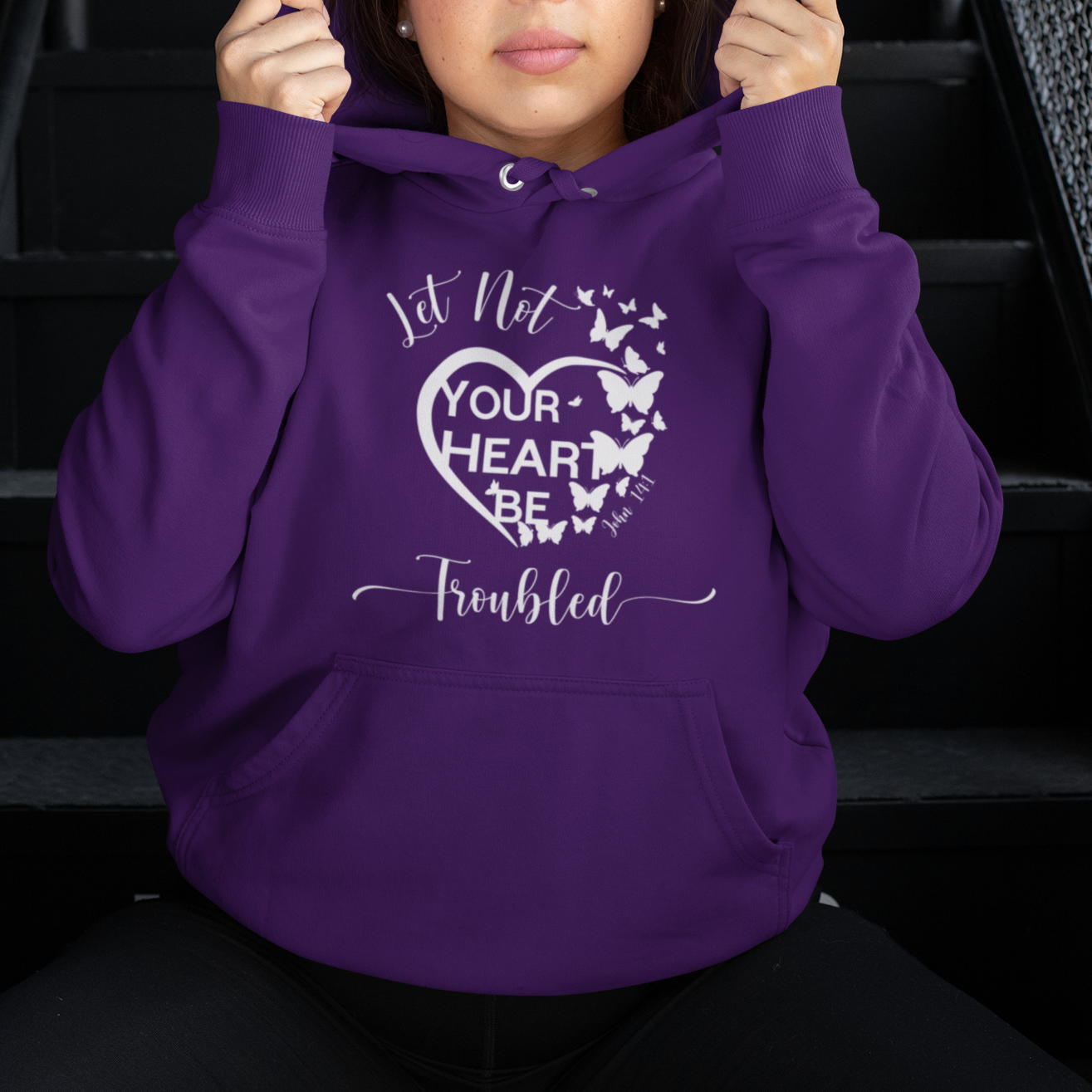 Person wearing a purple hoodie with text and butterfly design, sitting on stairs.