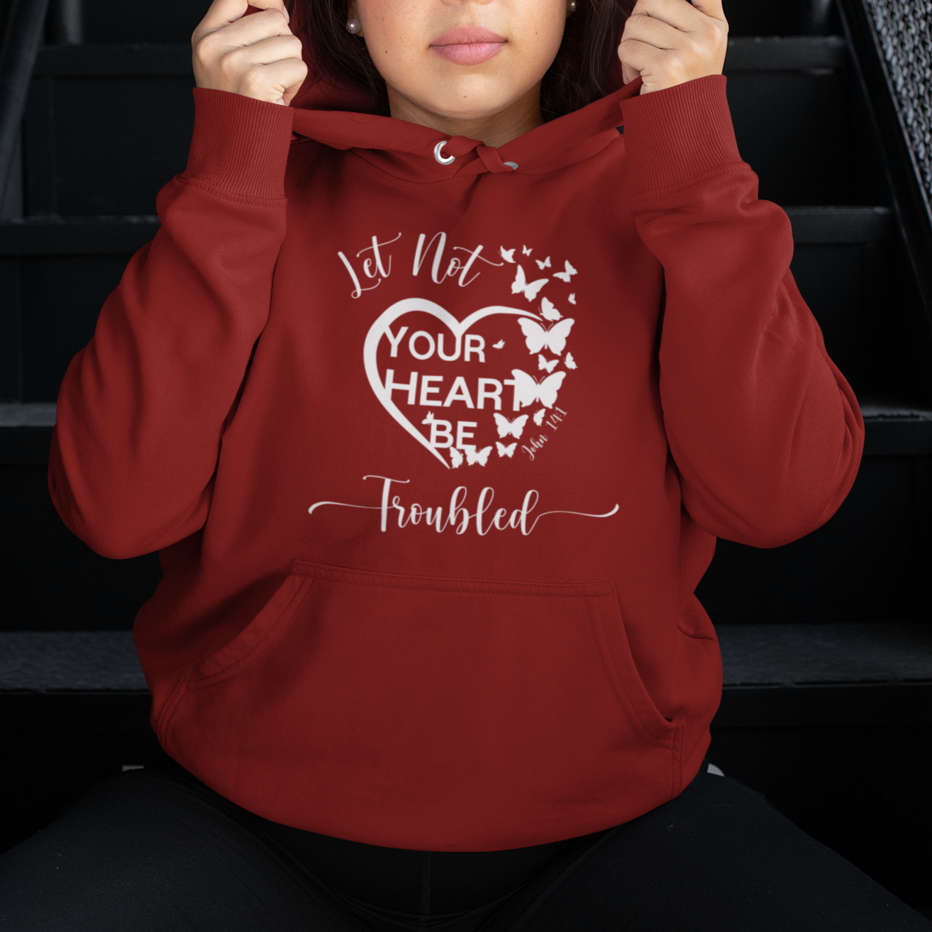 Person wearing a red hoodie with a heart design and text, sitting on stairs.