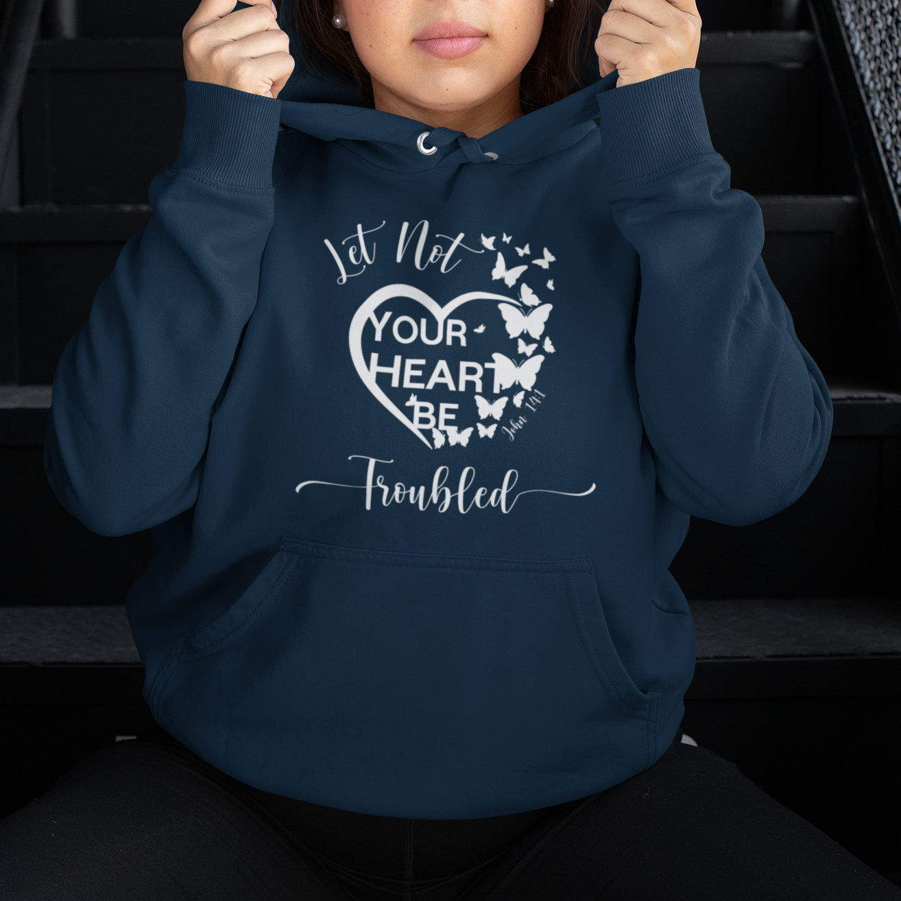 Person wearing a navy blue hoodie with text and butterfly design, sitting on stairs.
