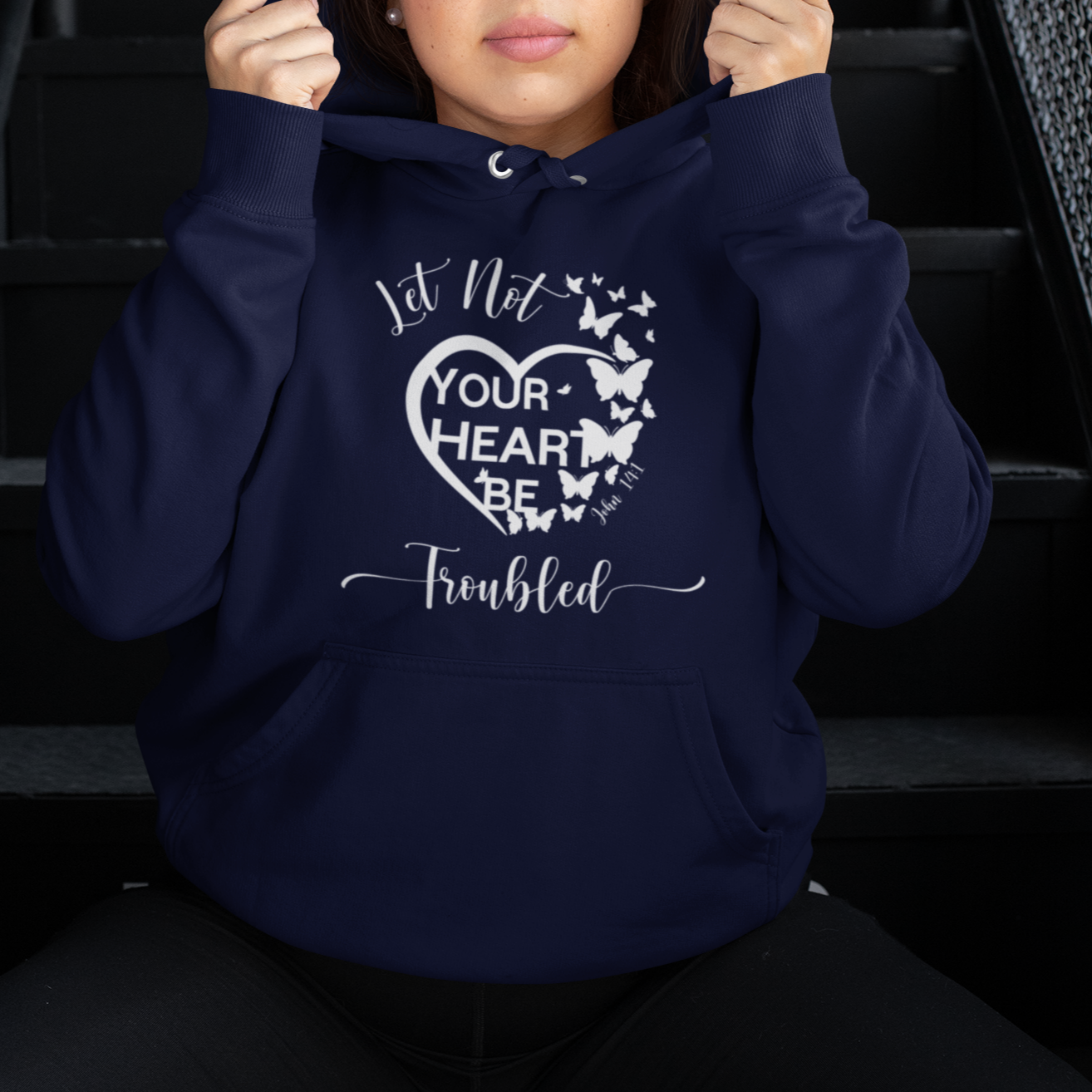 Person wearing a navy blue hoodie with text and butterfly design, sitting on stairs.