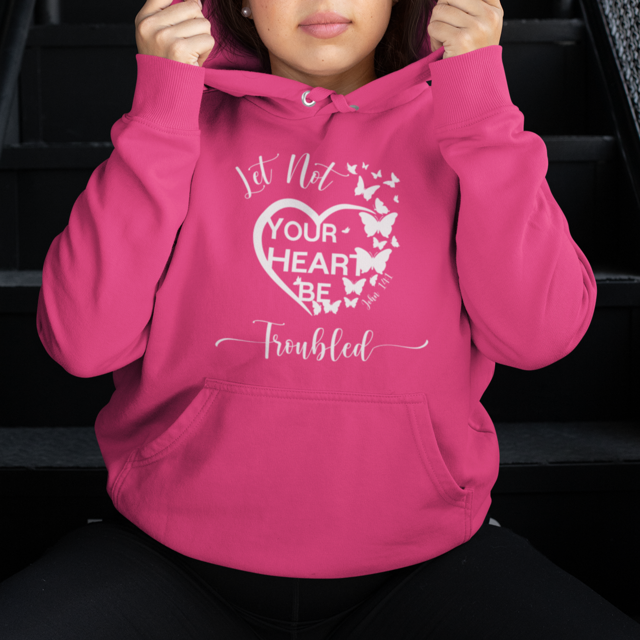 Person wearing a pink hoodie with text and butterfly design, sitting on stairs.