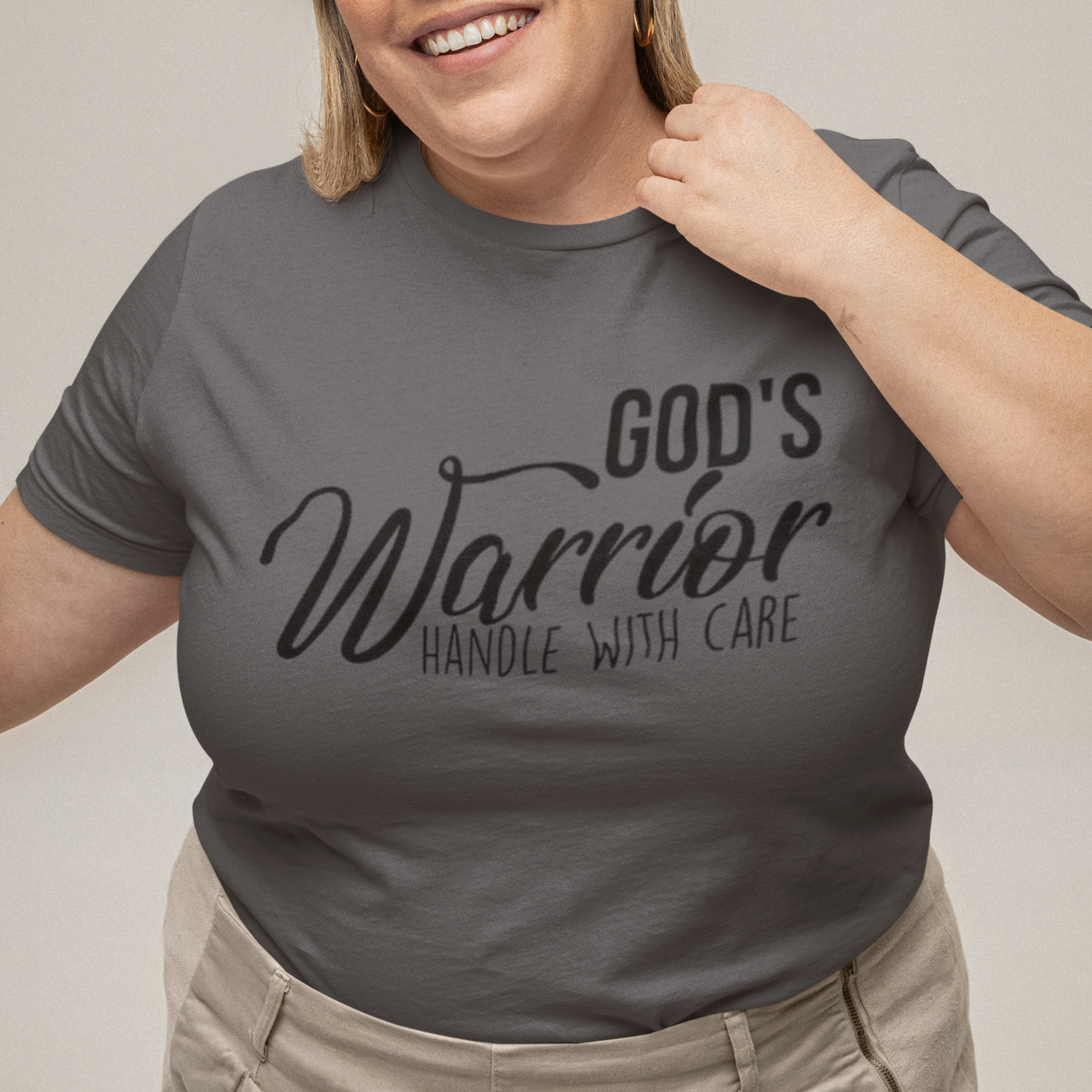 Person wearing a gray t-shirt with 'God's Warrior Handle with Care' text on a plain background