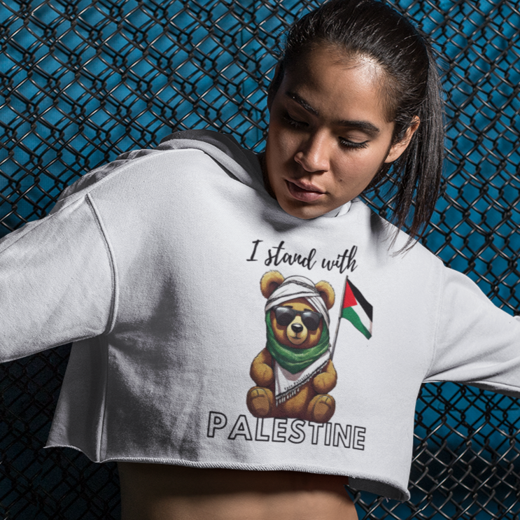 Person wearing a white sweatshirt with a bear graphic and text, standing against a blue chain-link fence.
