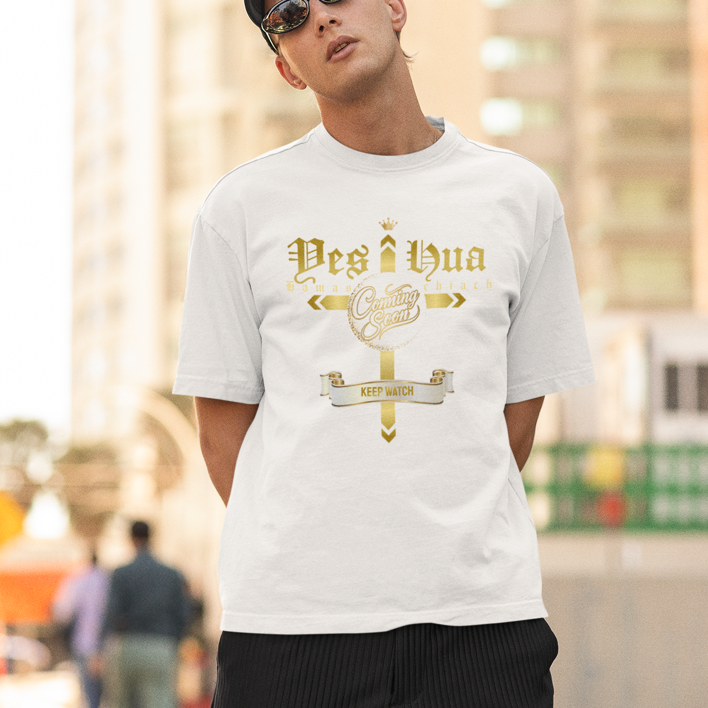 Man wearing a white t-shirt with gold text and sunglasses, standing outdoors.
