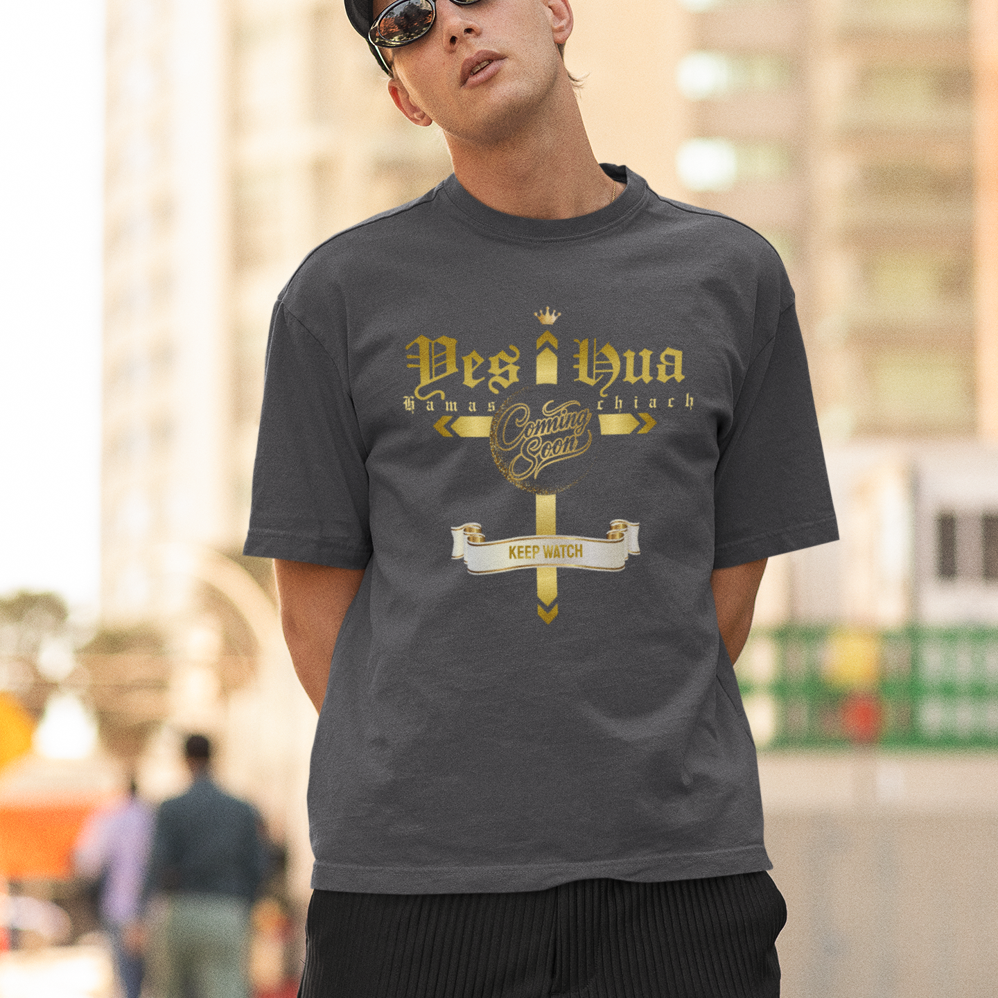 Man wearing a gray t-shirt with gold text and graphics outdoors.