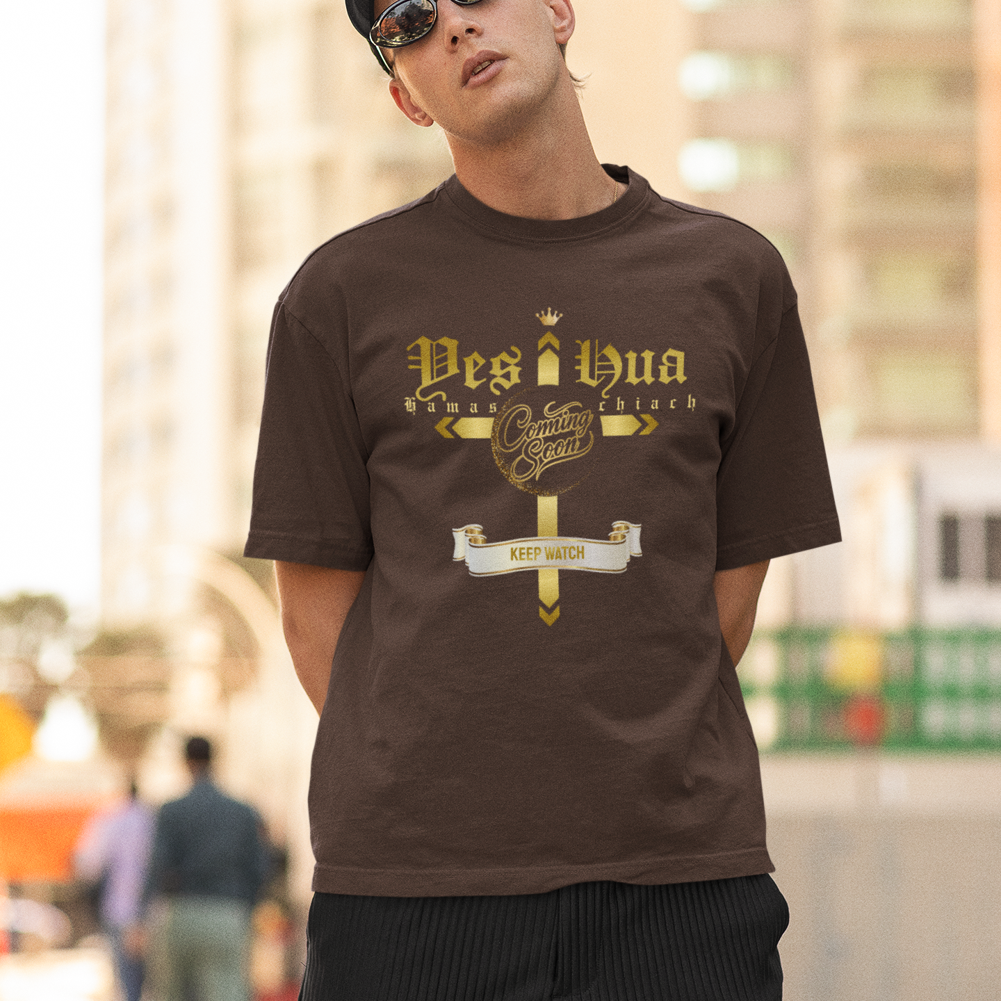Man wearing a brown t-shirt with a logo and text, standing outdoors.