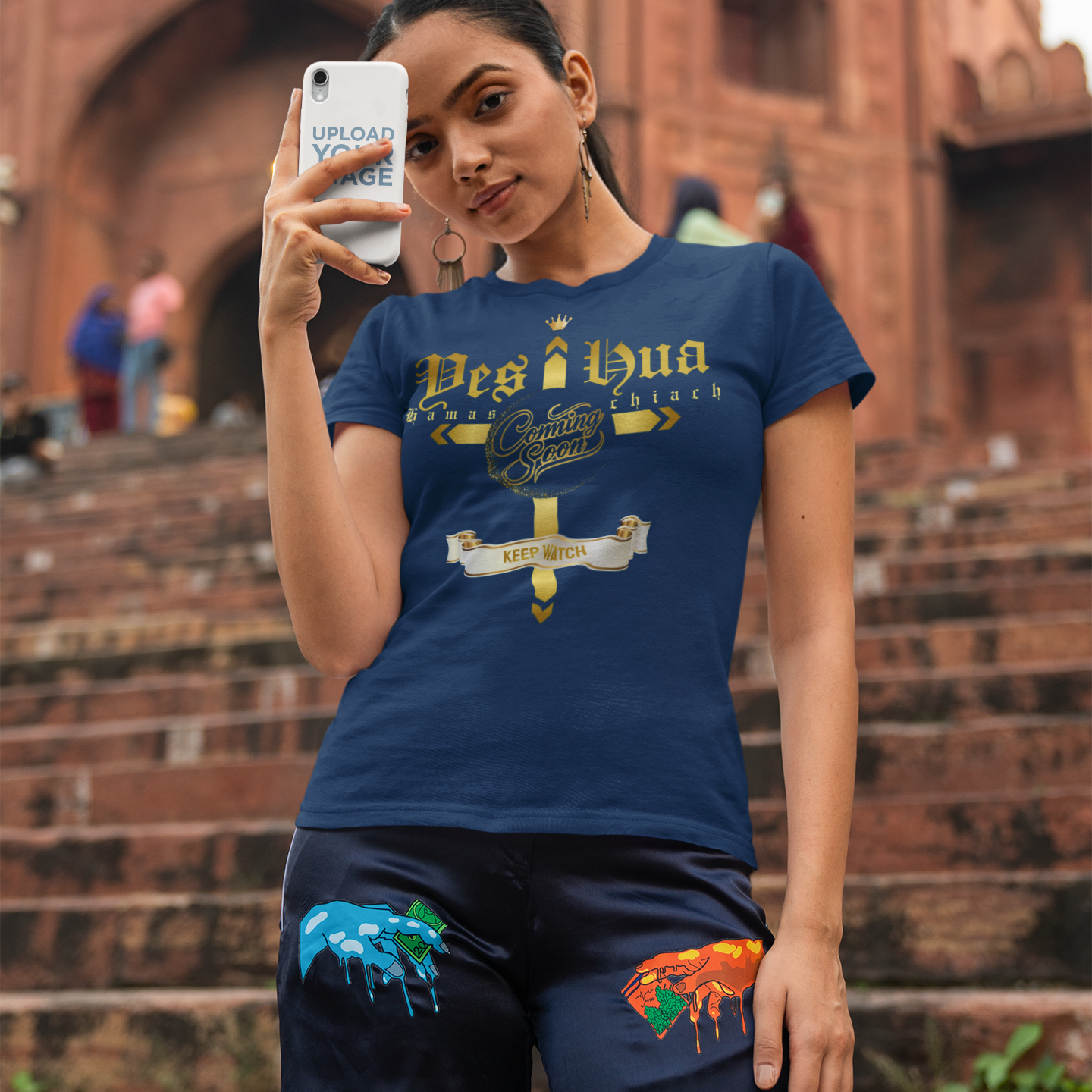 Woman taking a selfie in front of a historic building wearing a blue t-shirt with text and graphics.
