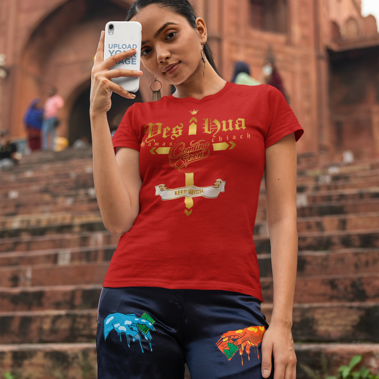 Person wearing a red t-shirt with a design, standing on steps with a brick building in the background.