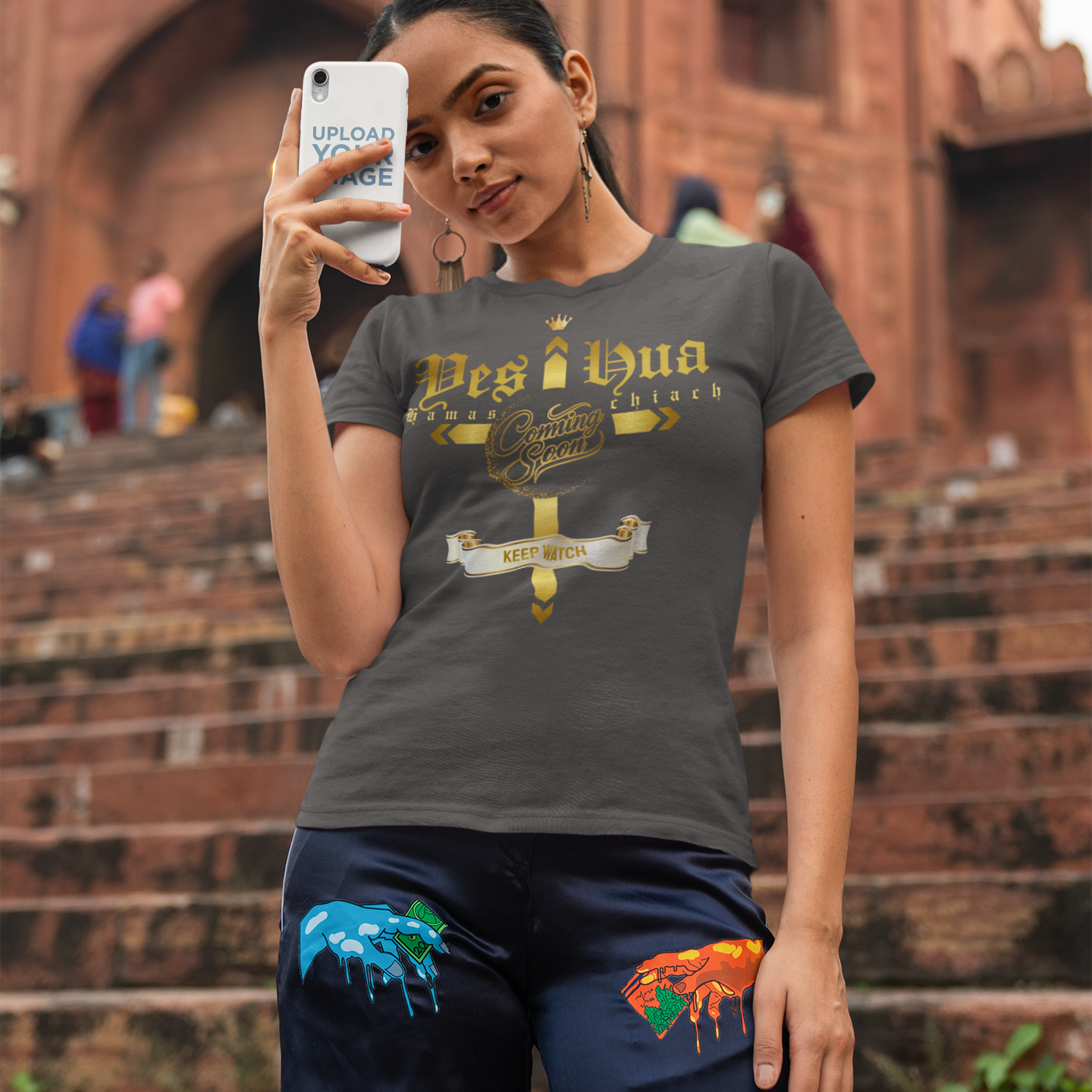 Woman taking a selfie in front of a historic building wearing a dark gray t-shirt with text and graphics.