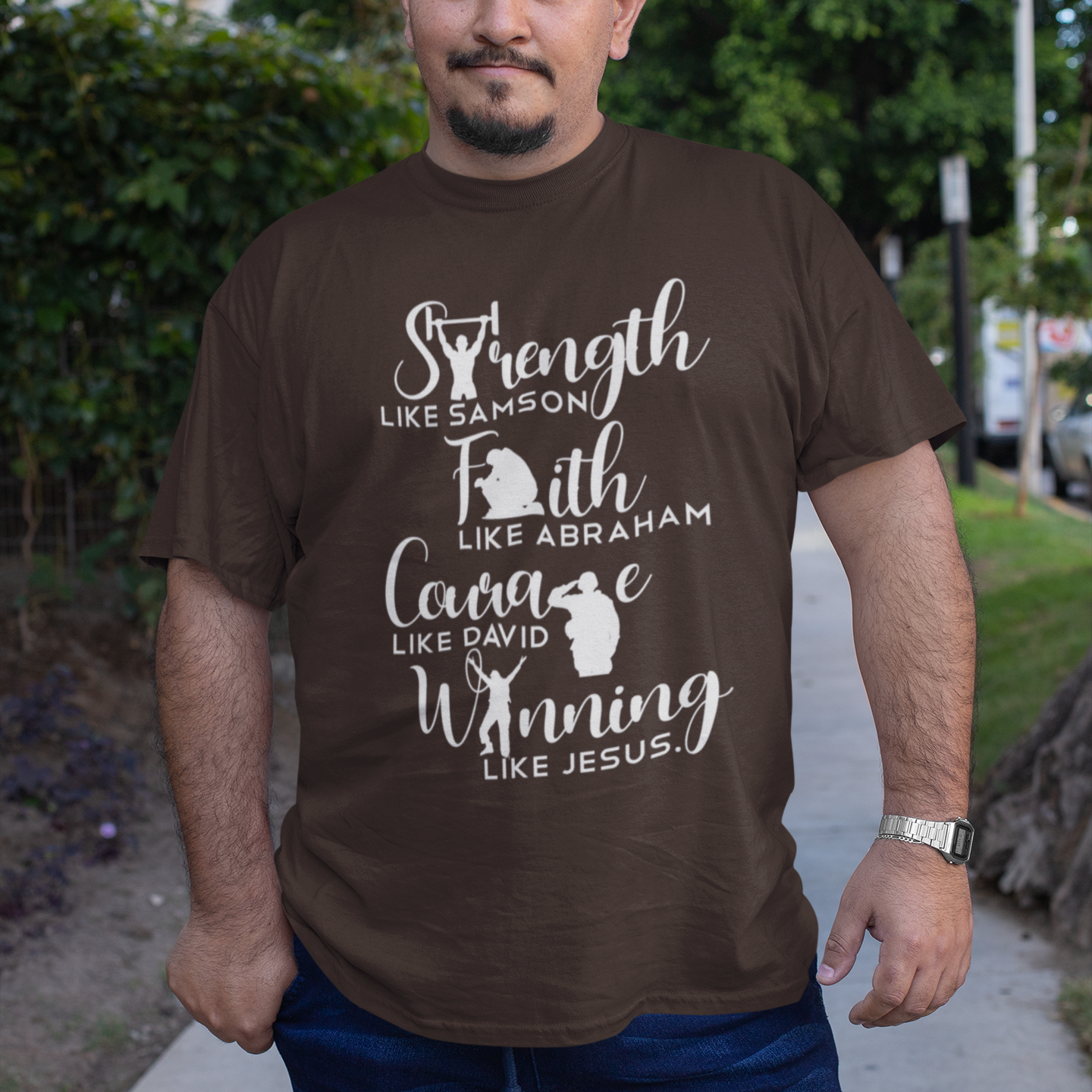 Man wearing a brown t-shirt with motivational text and graphics outdoors.