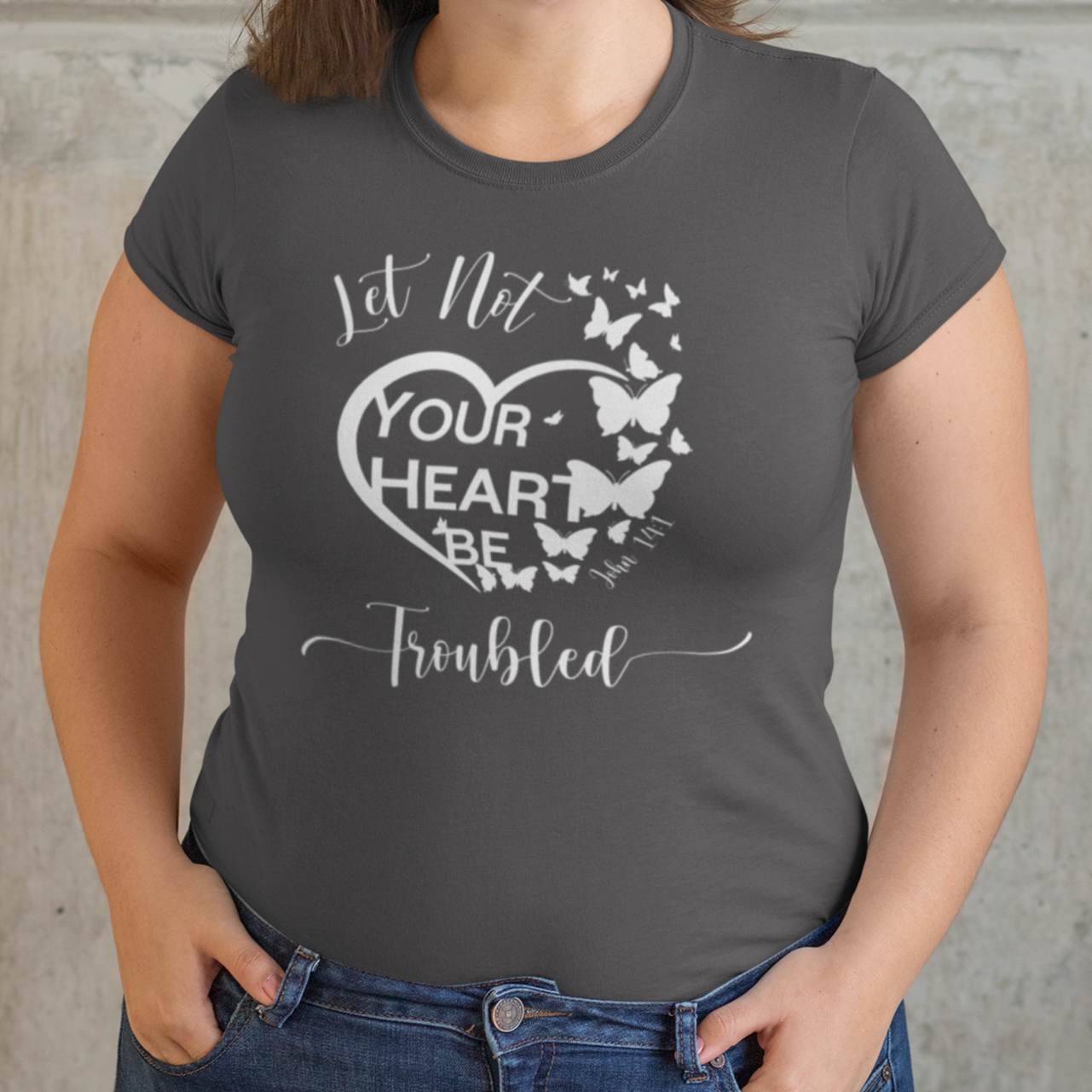 Woman wearing a gray t-shirt with a heart design and text against a stone wall.
