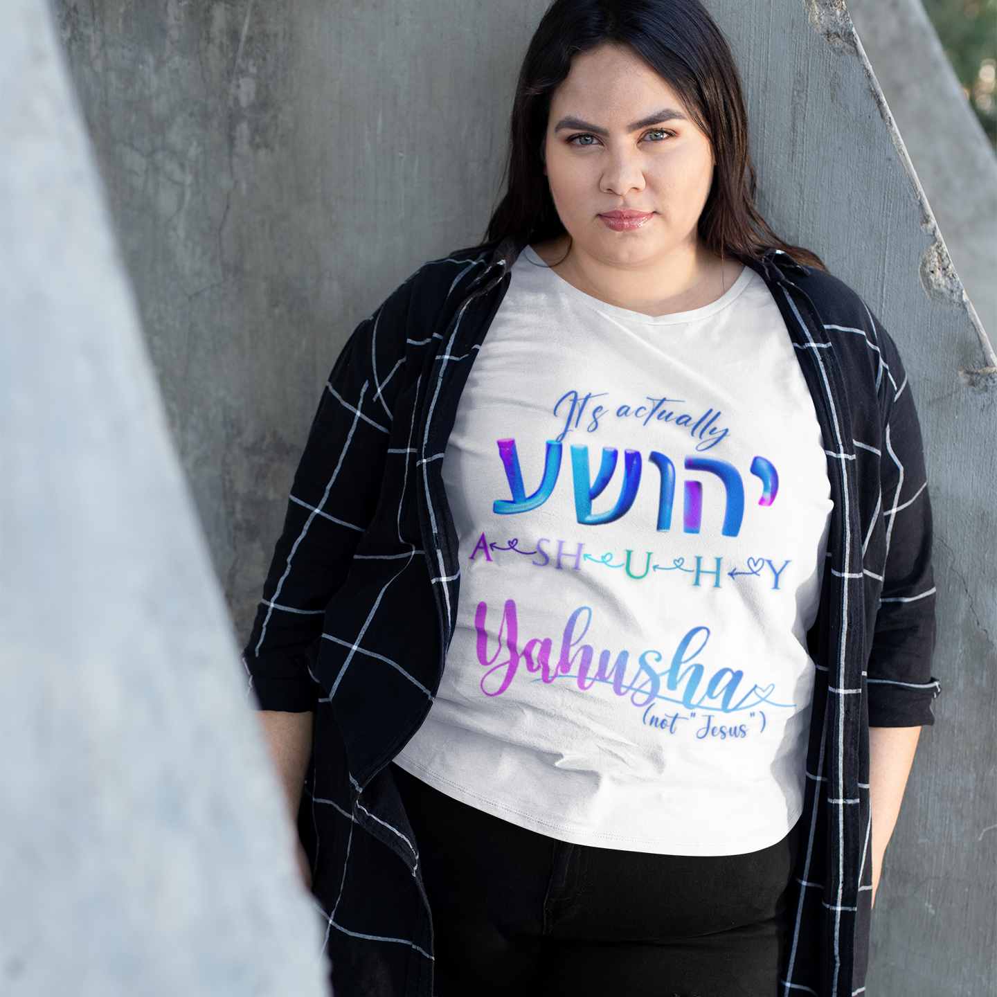 Person wearing a white t-shirt with colorful text, standing against a concrete wall.