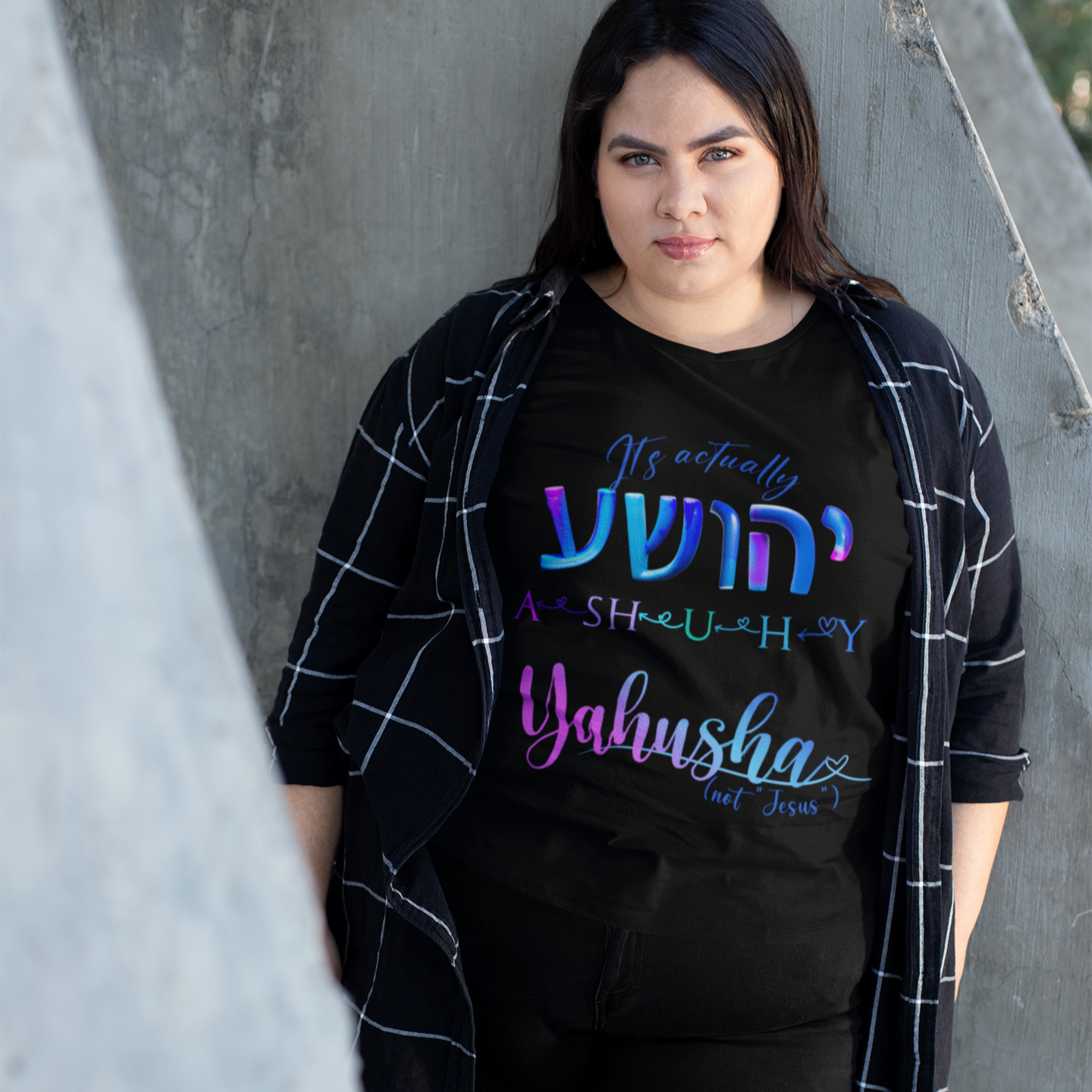 Person wearing a black t-shirt with colorful text, standing against a concrete wall.