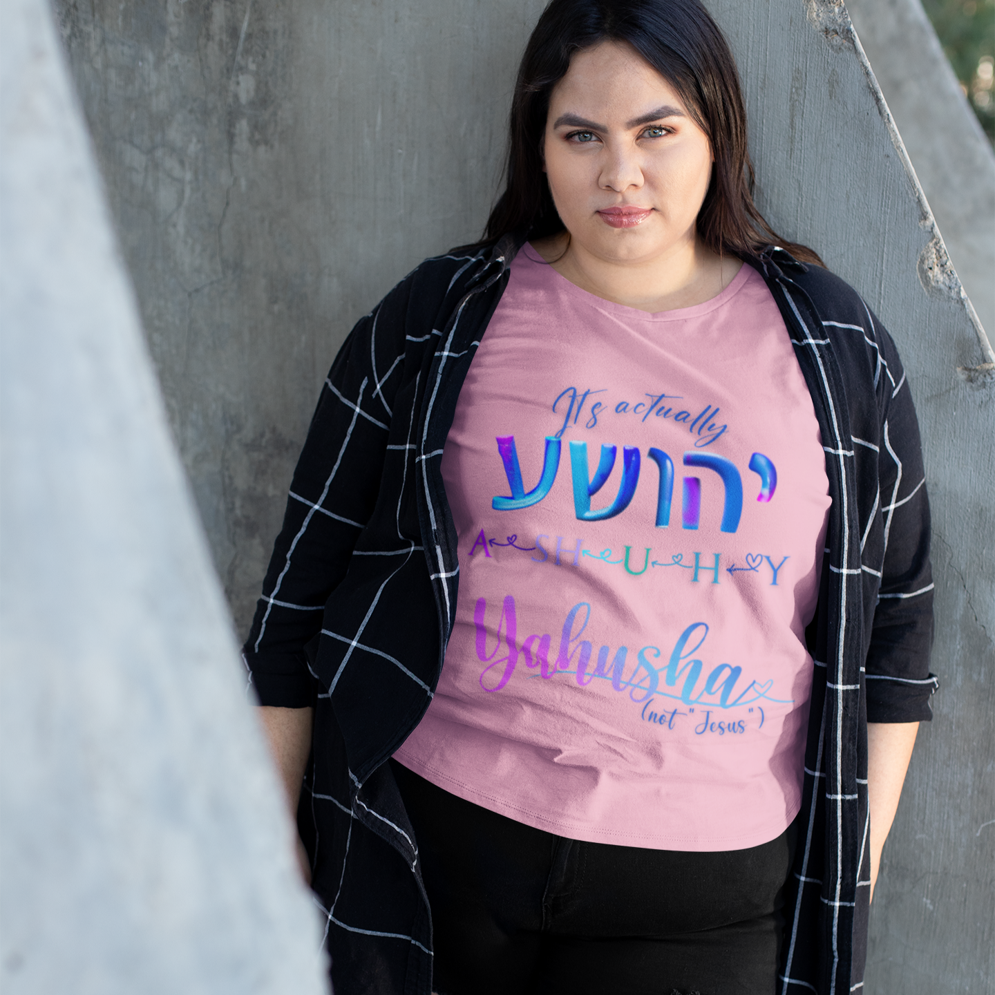 Person wearing a pink t-shirt with colorful text, standing against a concrete wall.