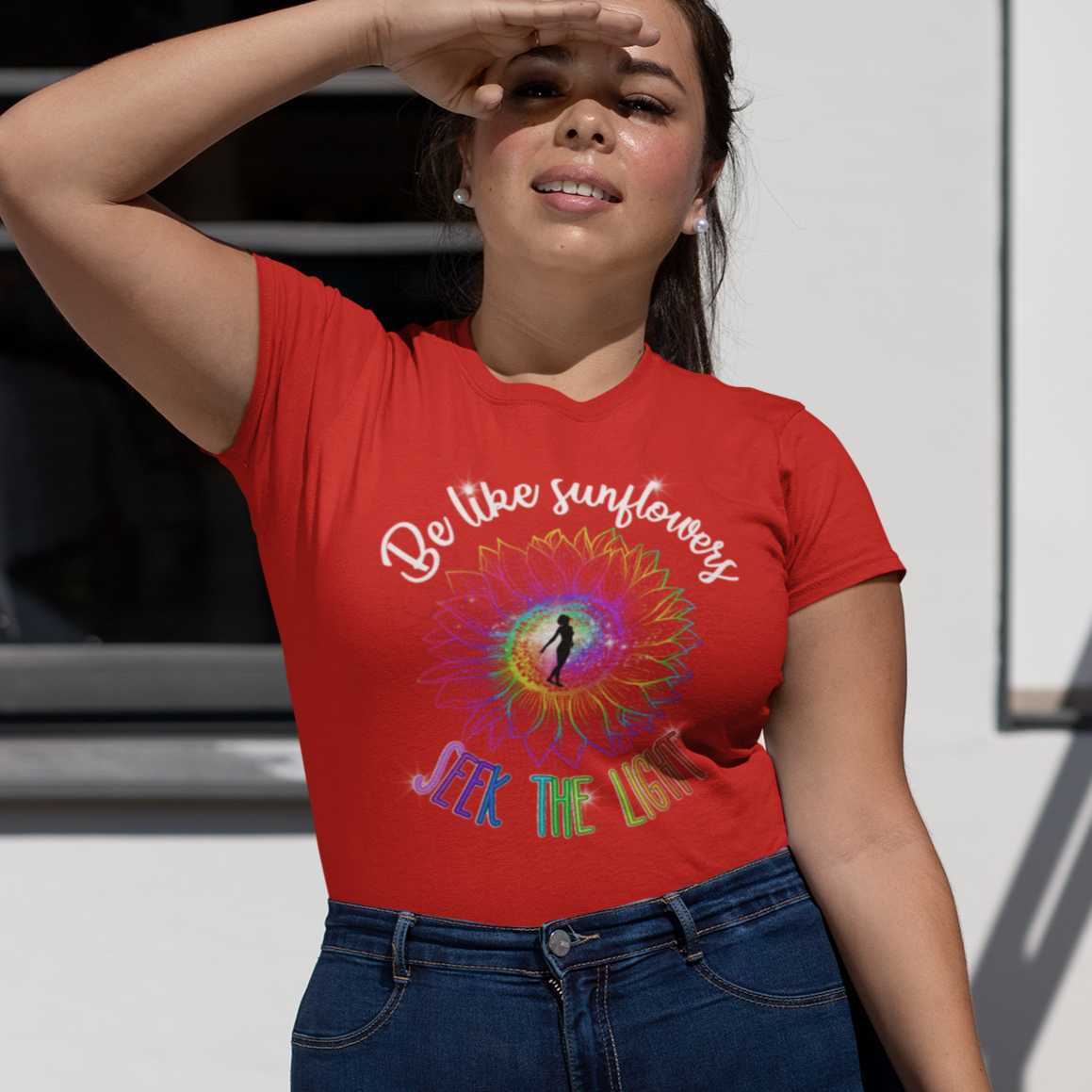 Woman wearing a red t-shirt with a colorful design and text, standing outdoors.
