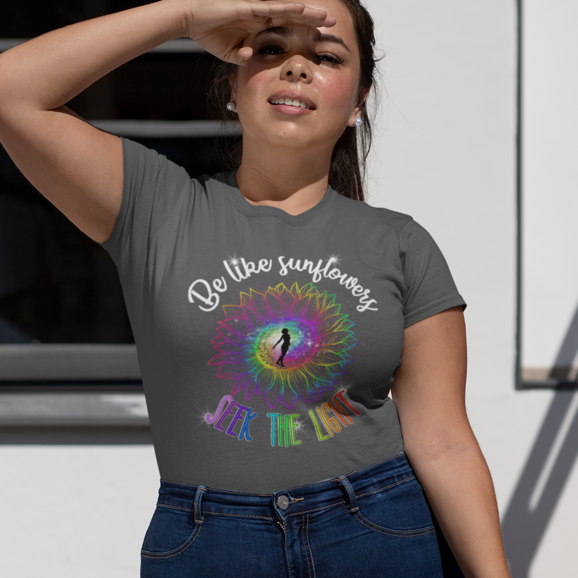 Woman wearing a gray t-shirt with a colorful design and text, standing outdoors.