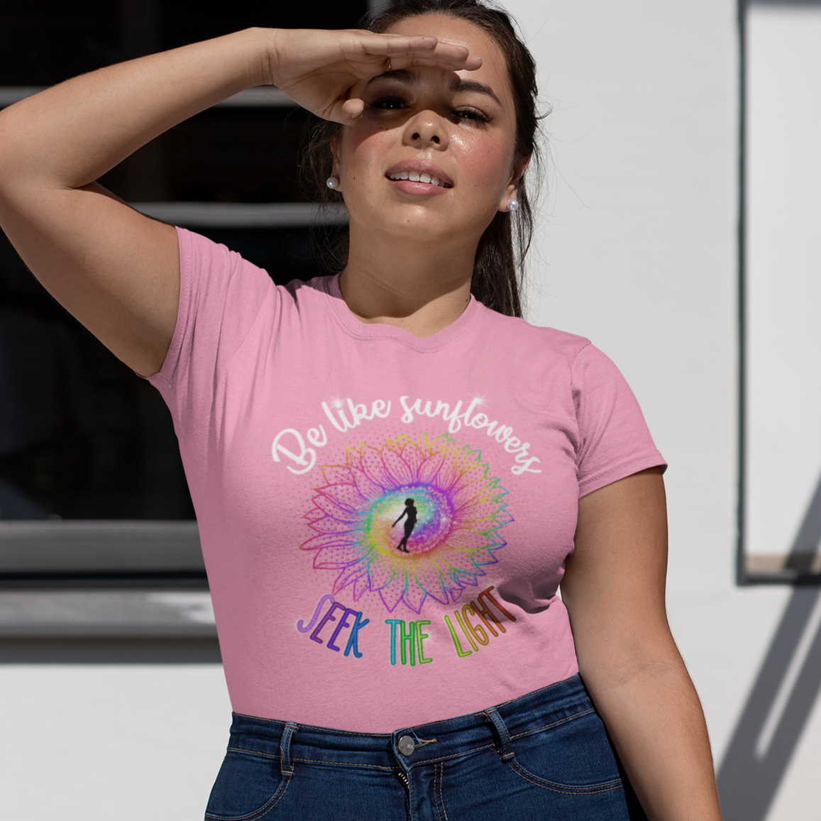 Woman wearing a pink t-shirt with a colorful design and text, standing outdoors.