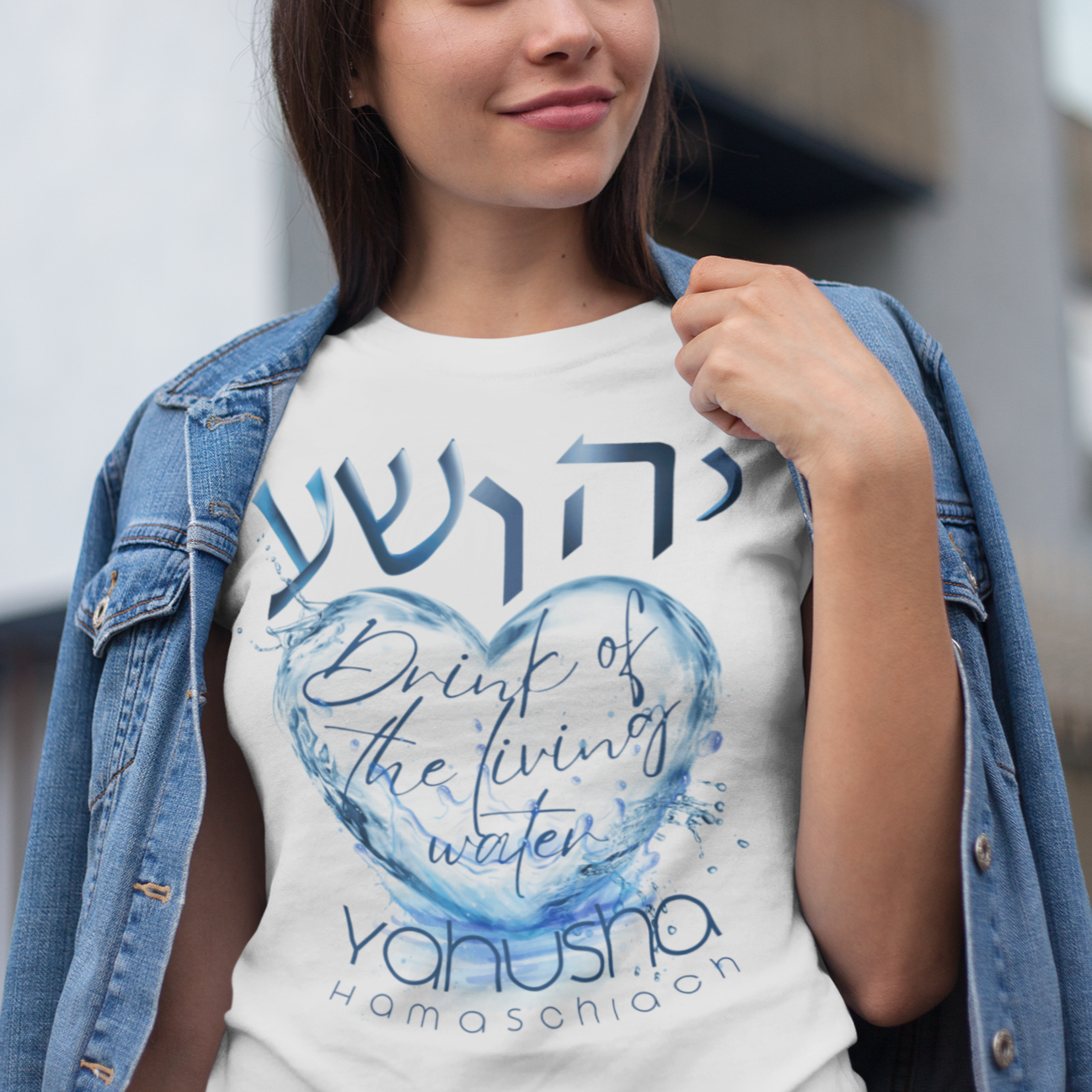 Woman wearing a white t-shirt with blue text and design, standing outdoors.