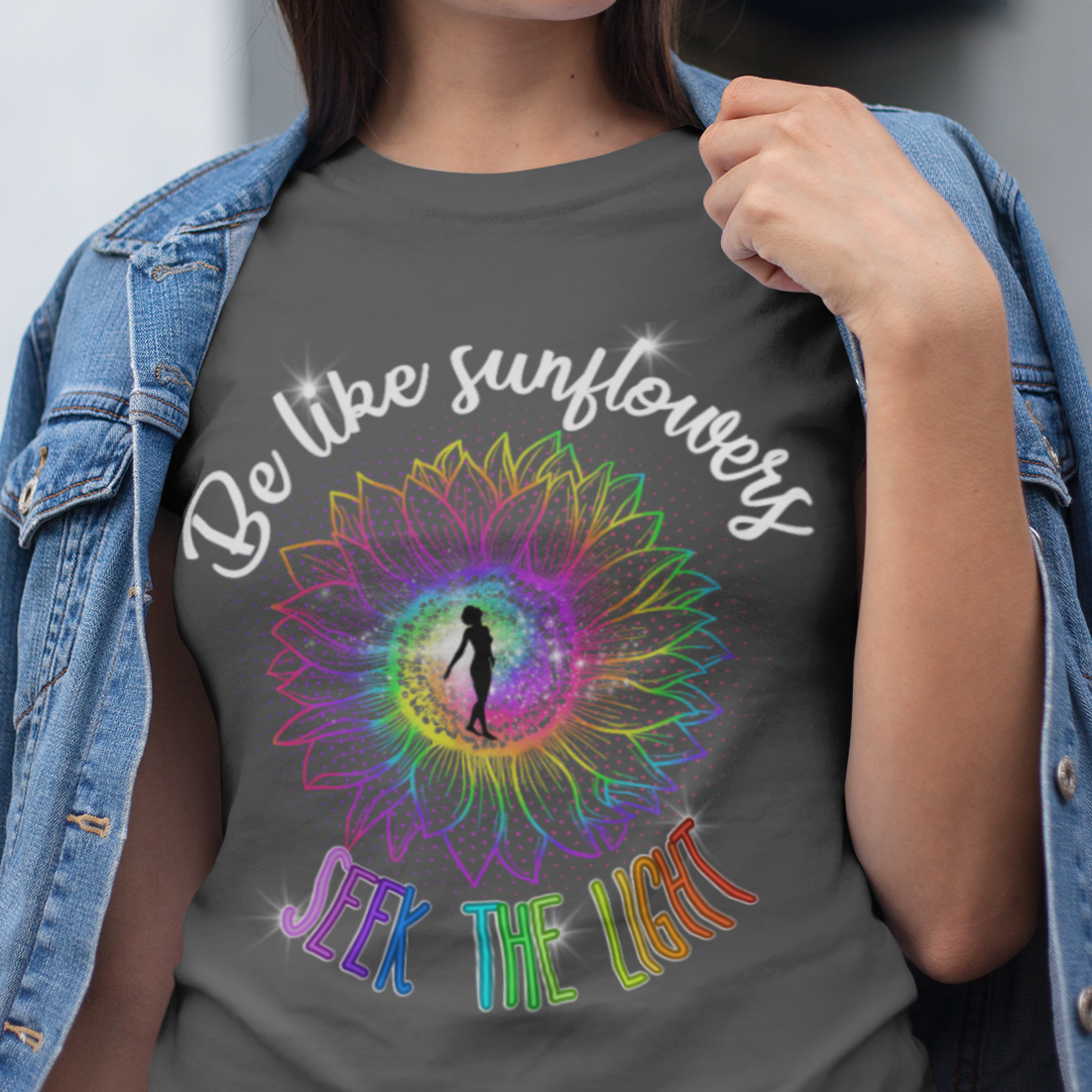 Woman wearing a gray t-shirt with a colorful design and text, standing outdoors.