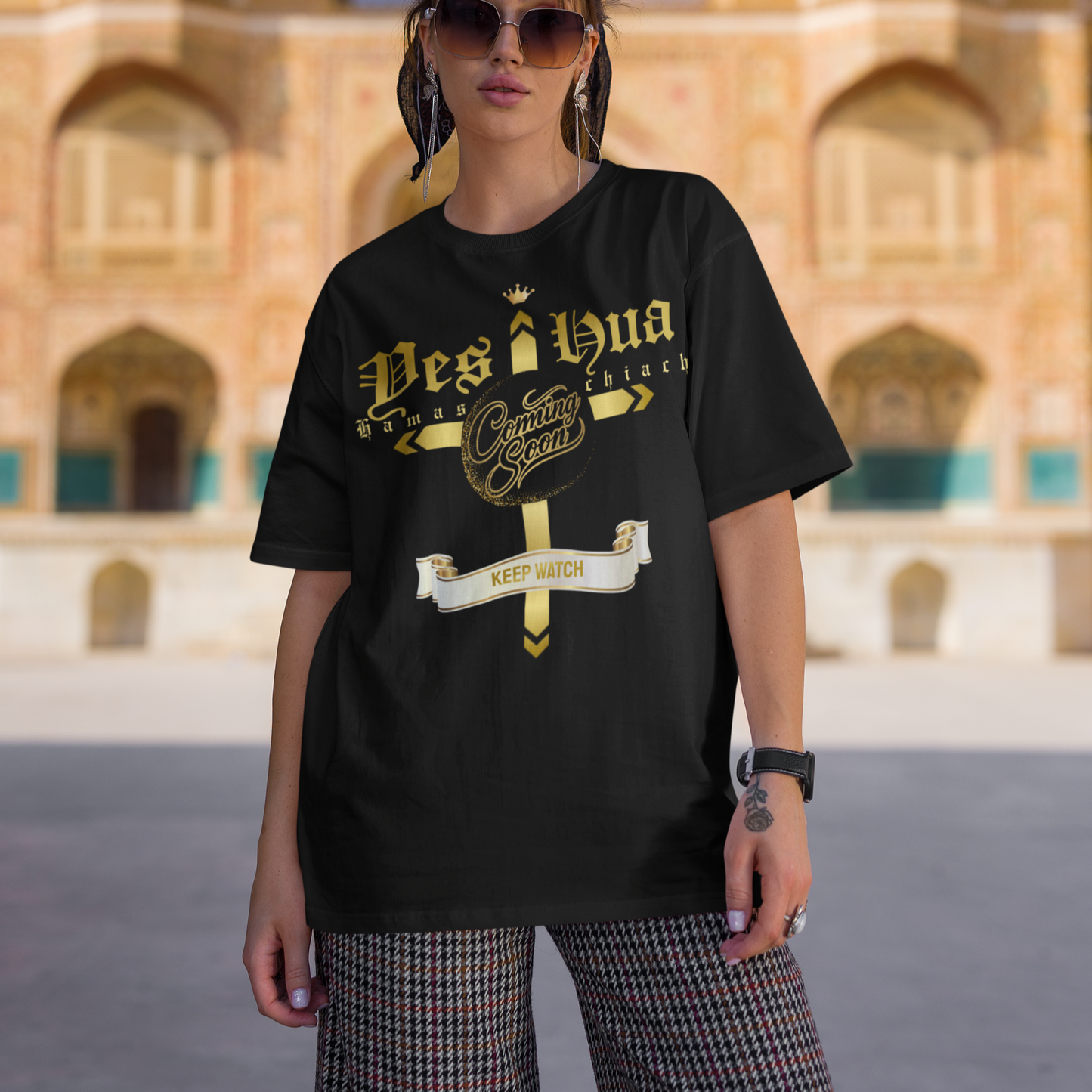 Person wearing a black t-shirt with gold text in front of an architectural building.