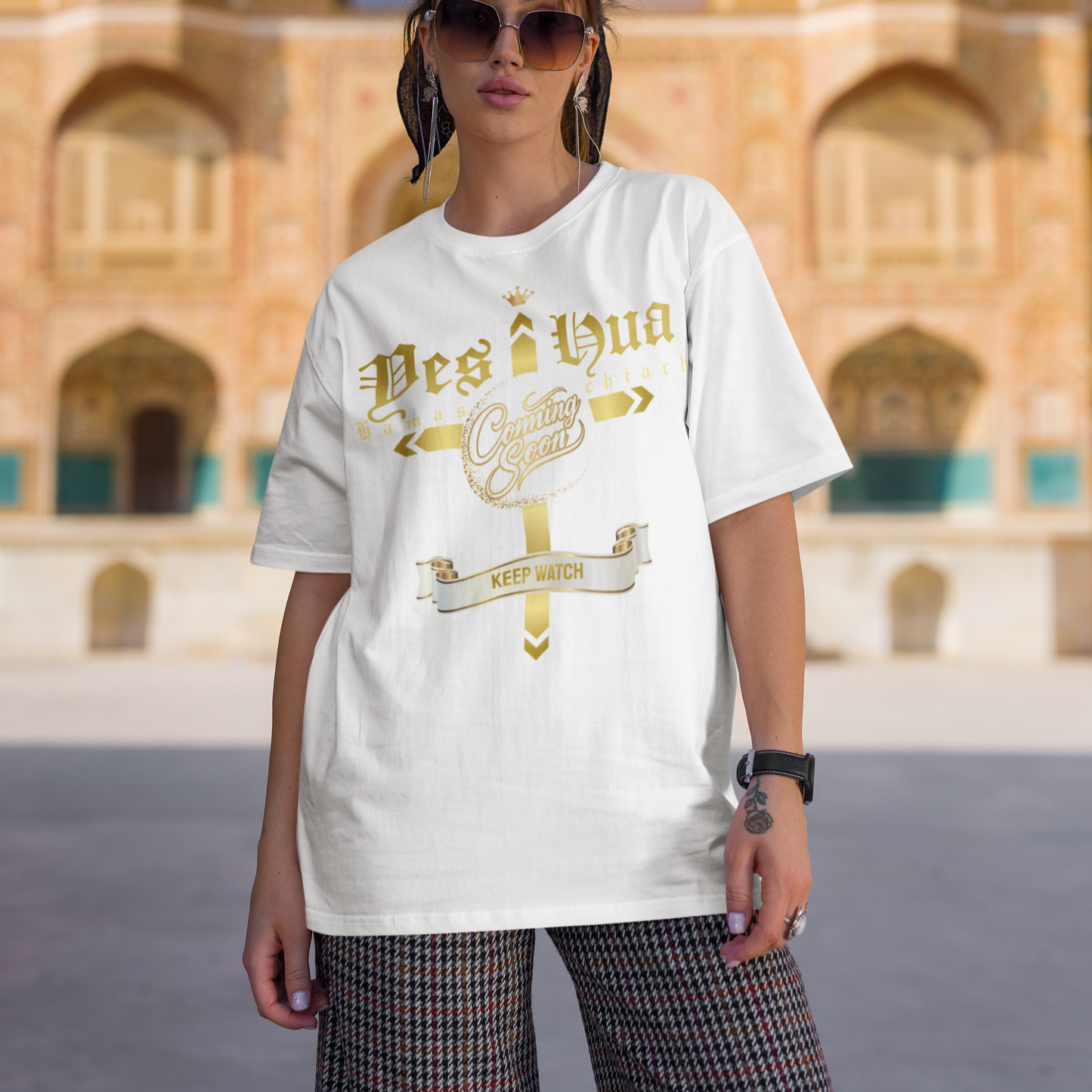 Person wearing a white t-shirt with gold text in front of an architectural building.