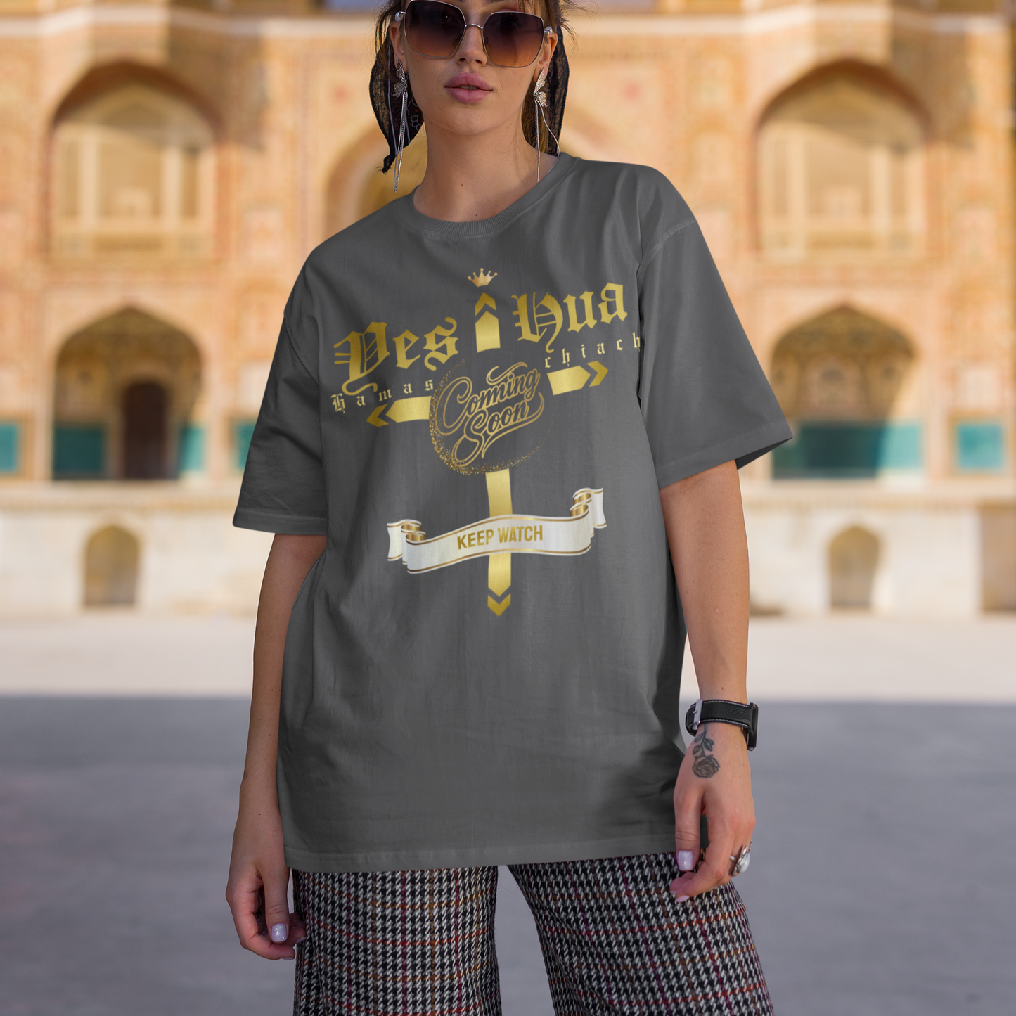Woman wearing a gray t-shirt with gold text in front of an architectural building.