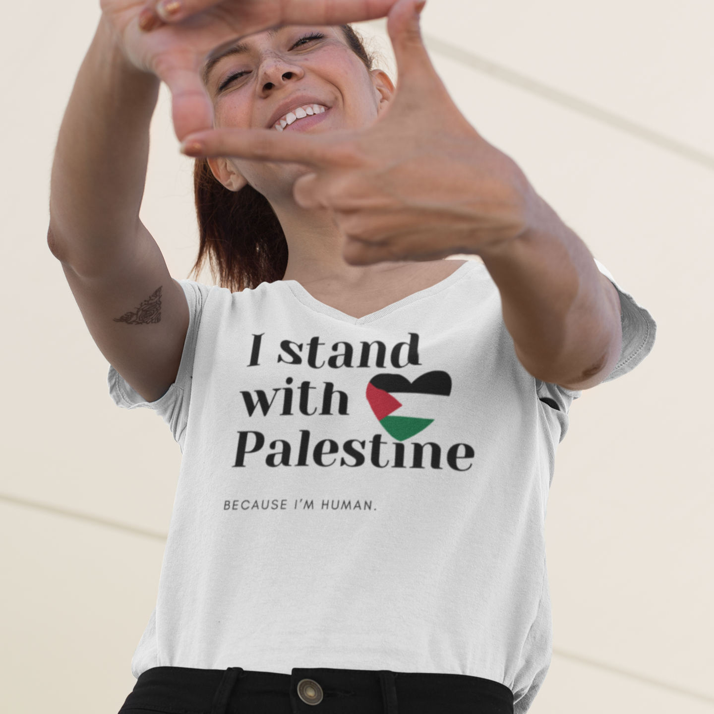 Person wearing a white t-shirt with 'I stand with Palestine because I'm human' text and a heart with a flag design, making a peace sign.