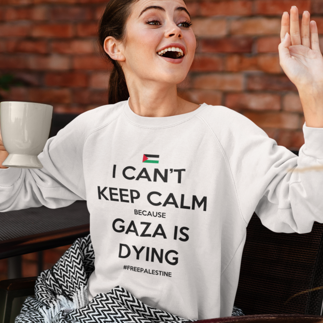 Woman wearing a sweatshirt with a message about Gaza, holding a mug, and sitting in front of a brick wall.