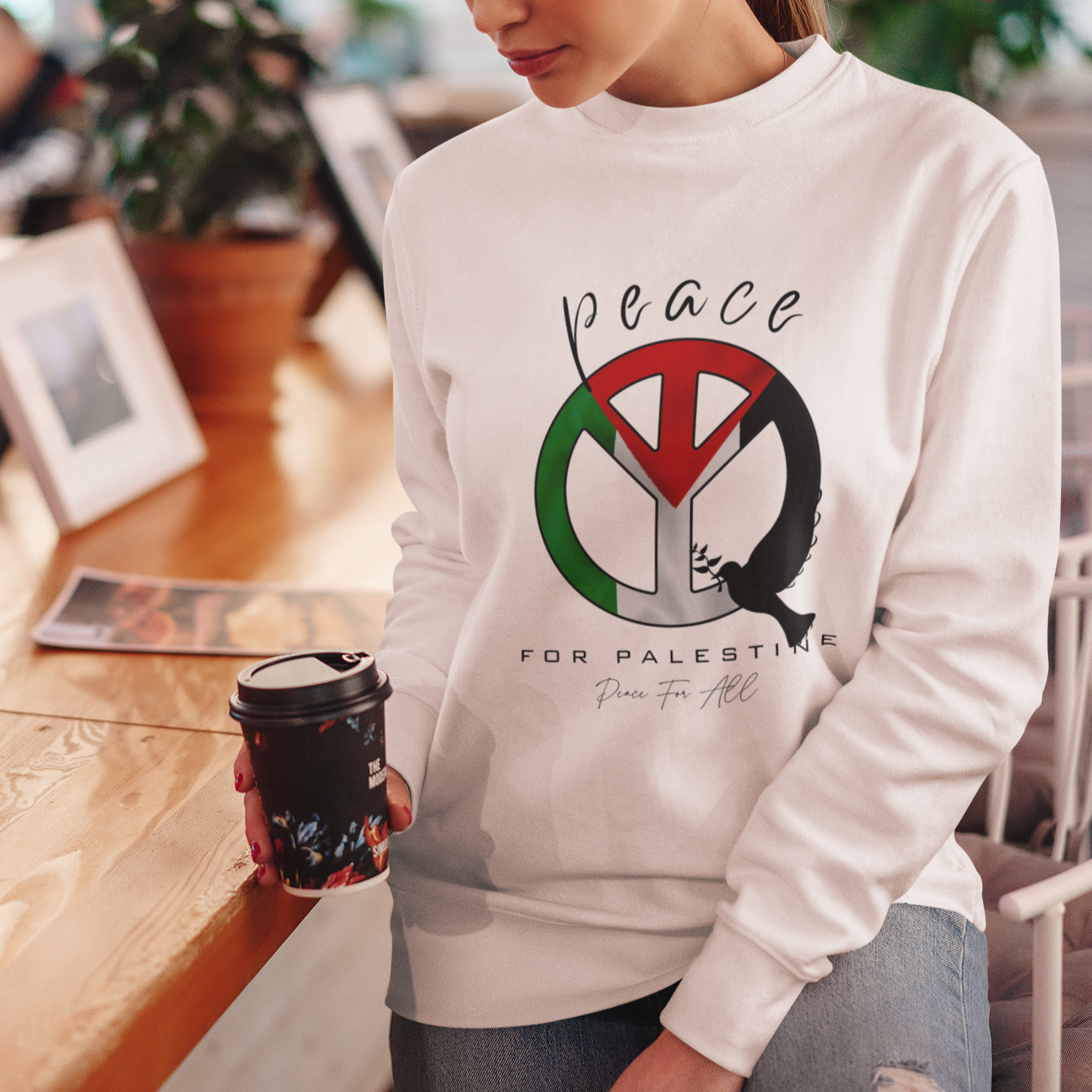 Woman wearing a white sweatshirt with a peace symbol design, standing in a casual setting.
