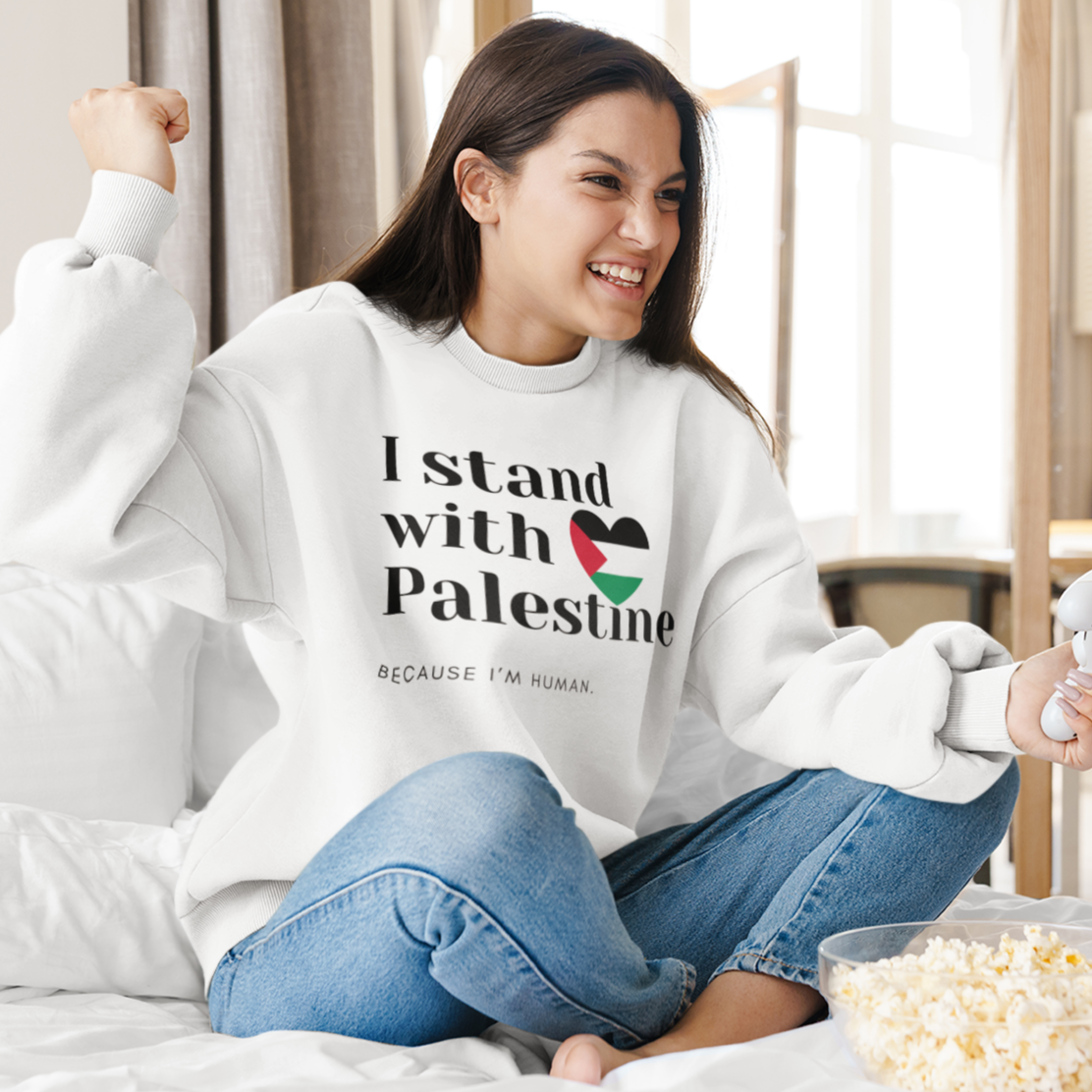 Woman wearing a sweatshirt with 'I stand with Palestine' text, sitting on a bed with popcorn.