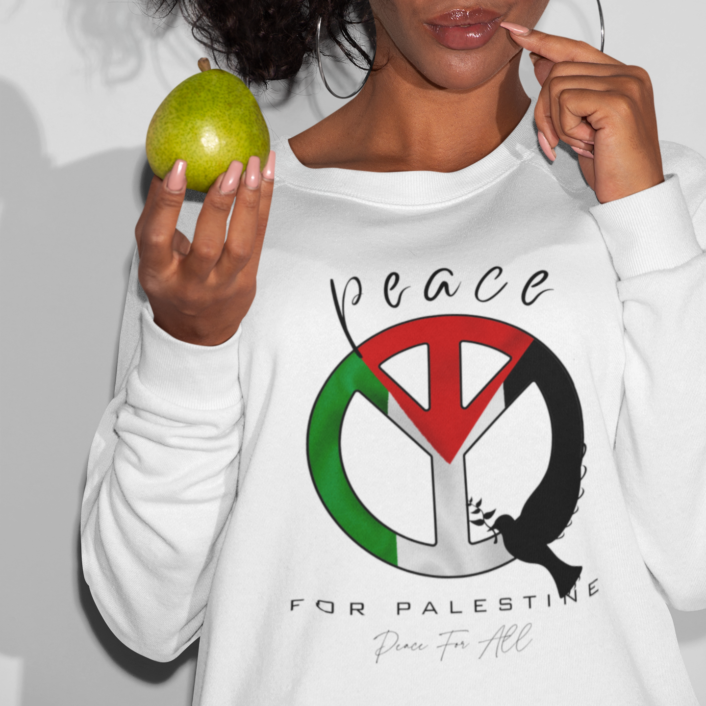 Person wearing a white sweatshirt with a peace symbol design, holding an apple.