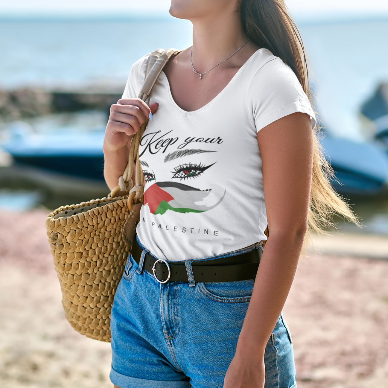 Woman on a beach wearing a white t-shirt with text and graphics, blue shorts, and sunglasses.