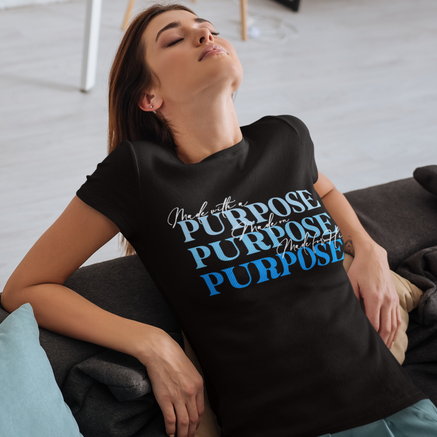 Woman wearing a black t-shirt with 'Purpose' text in different languages, sitting on a couch.