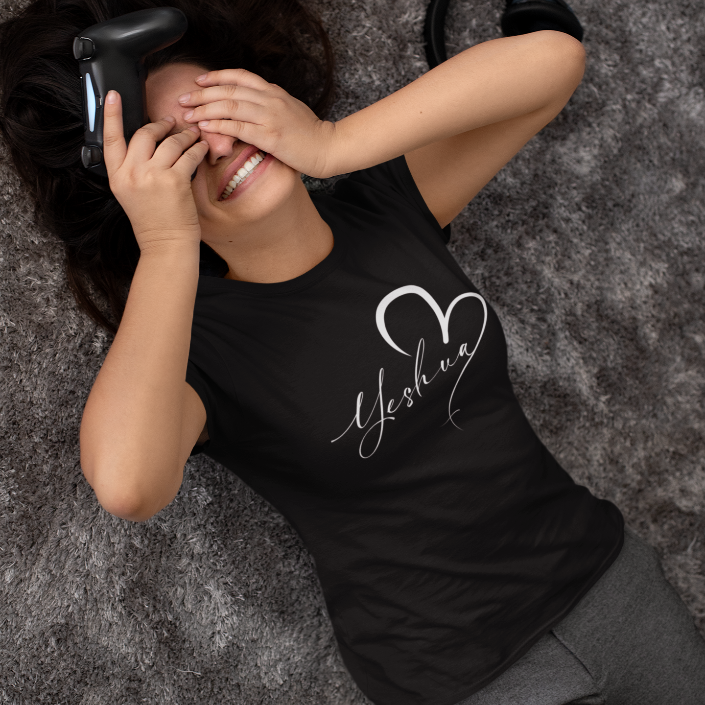 Person wearing a black t-shirt with 'Yeshu' design, lying on a textured surface.