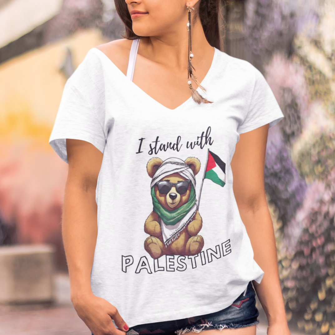 Woman wearing a white t-shirt with a bear graphic and 'I stand with Palestine' text, standing in front of a colorful mural.