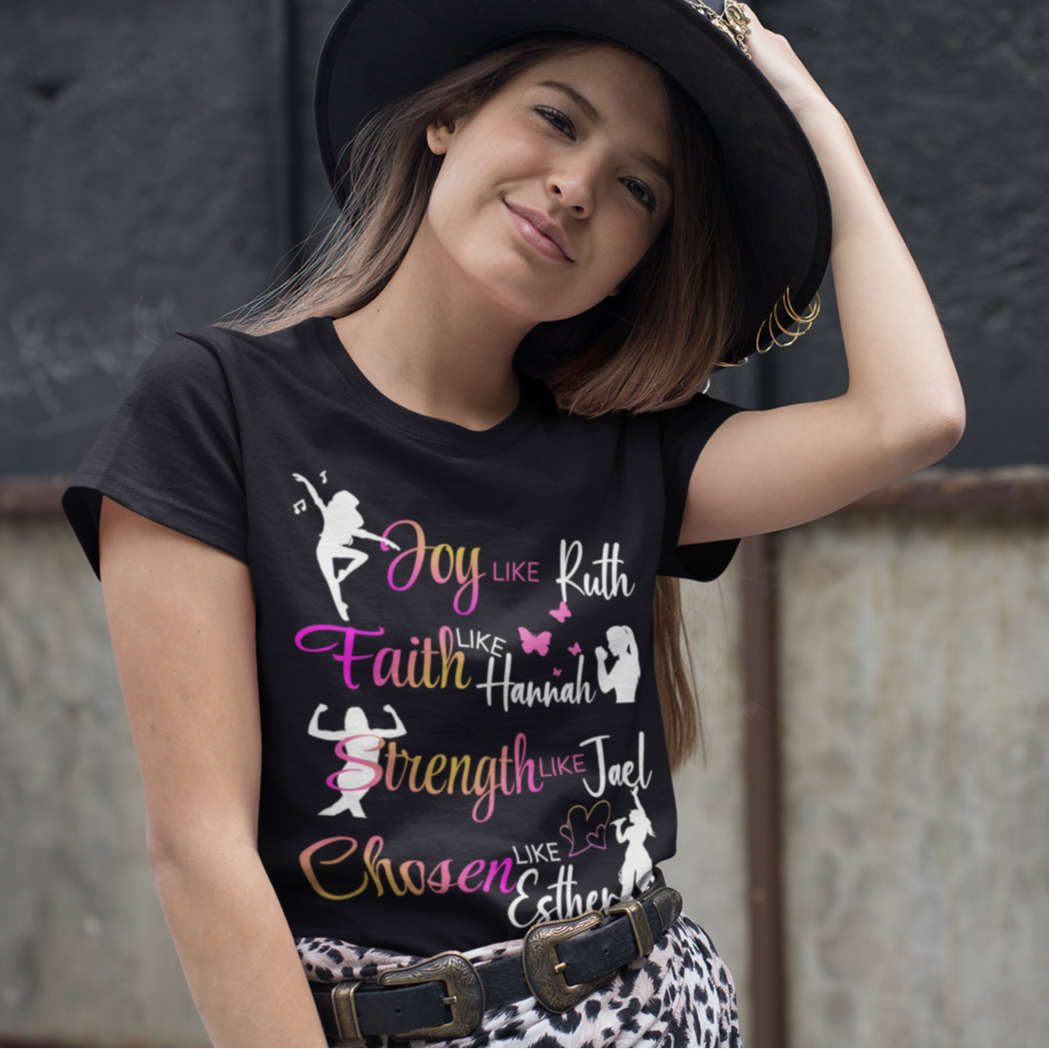 Woman wearing a black t-shirt with colorful text and graphics, standing against a textured wall.
