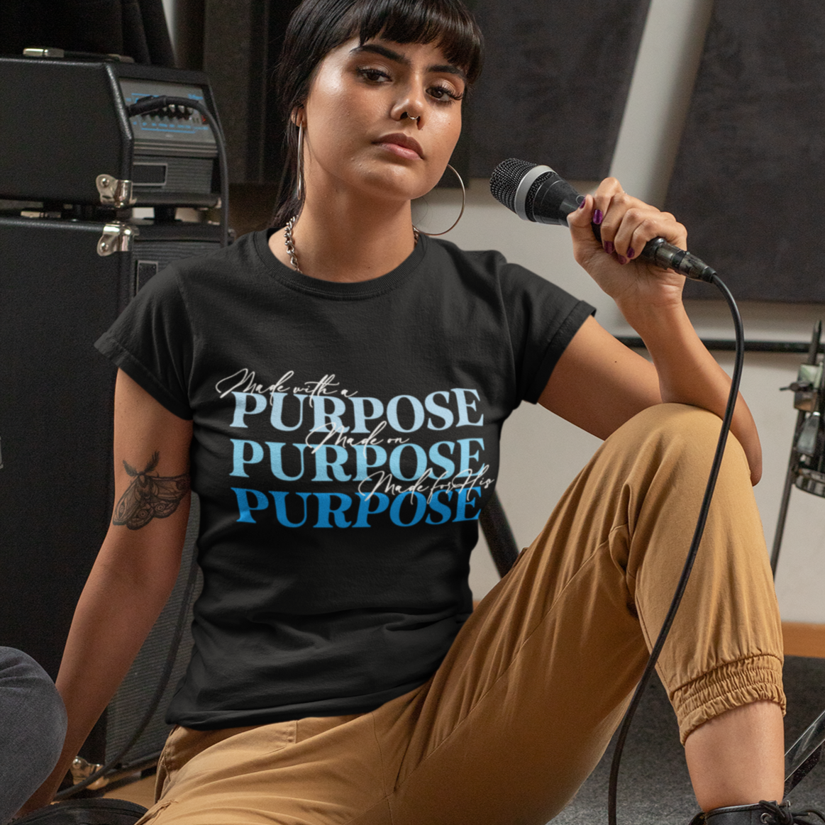 Person sitting on a stage with musical equipment, wearing a black t-shirt with text.