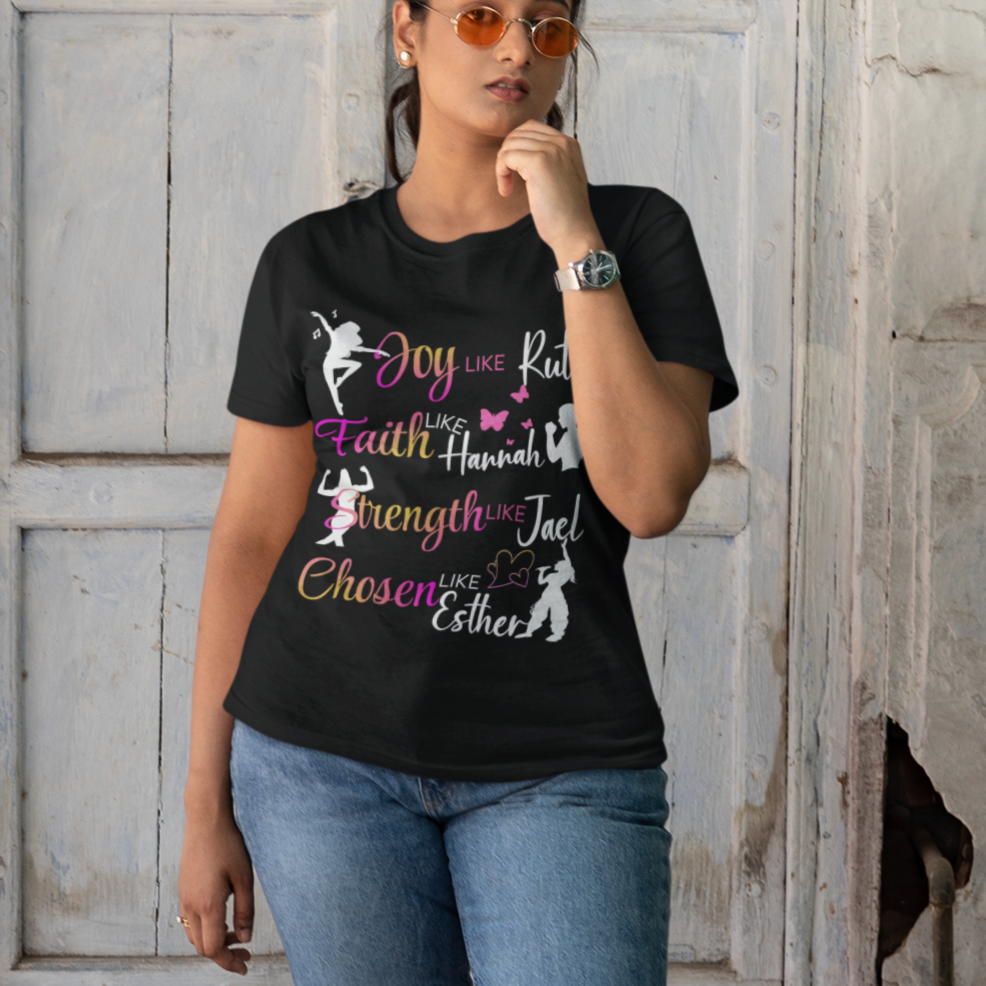 Woman wearing a black t-shirt with colorful text and graphics, standing in front of a rustic wooden door.