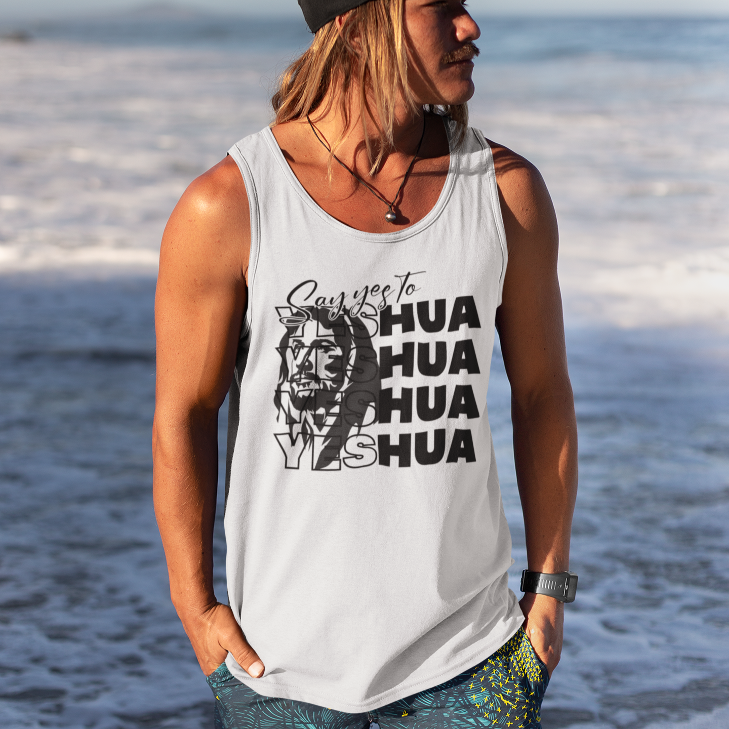 Person wearing a white tank top with text and graphics, standing on a beach.