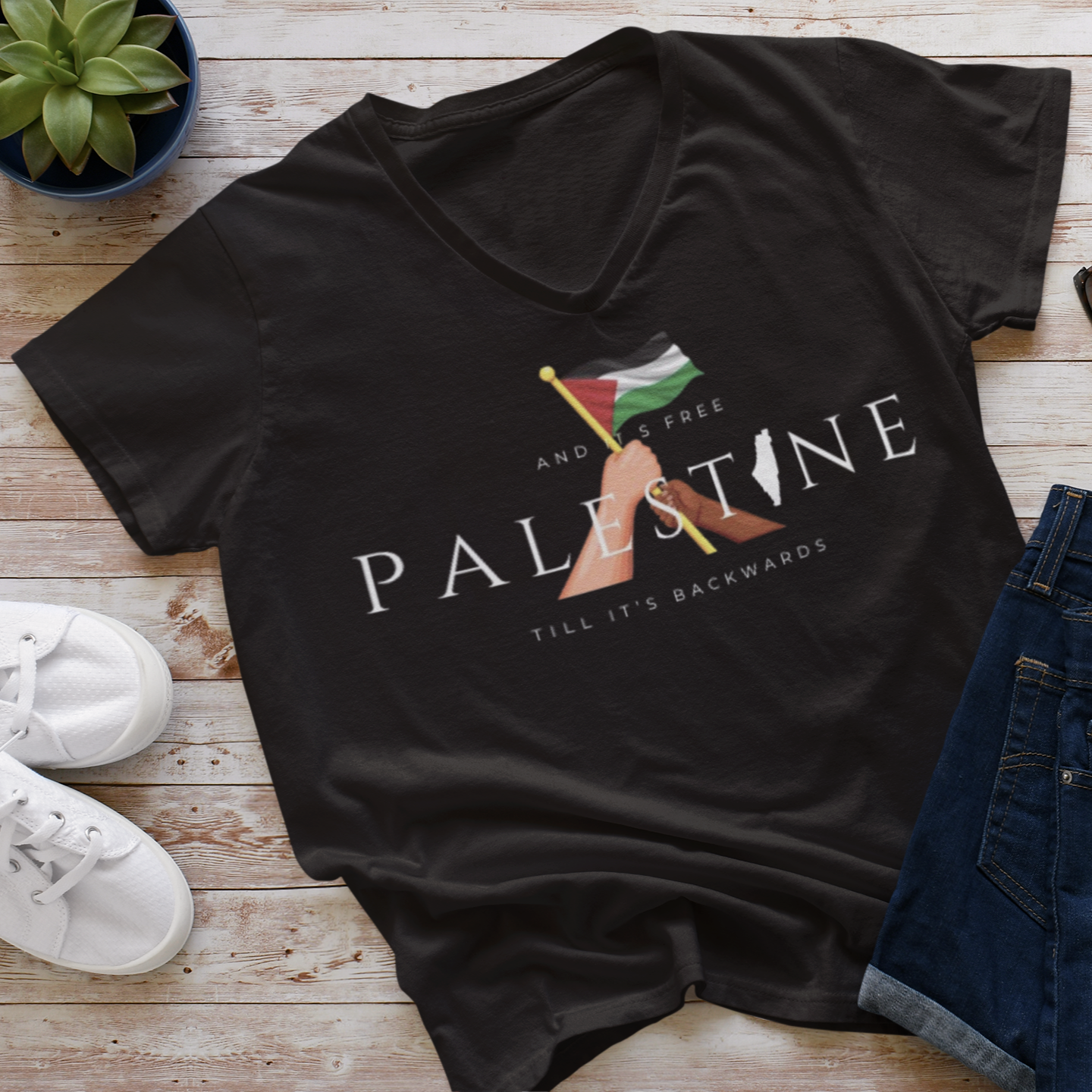 Black t-shirt with 'Free Palestine' design on a wooden surface with shoes and sunglasses.