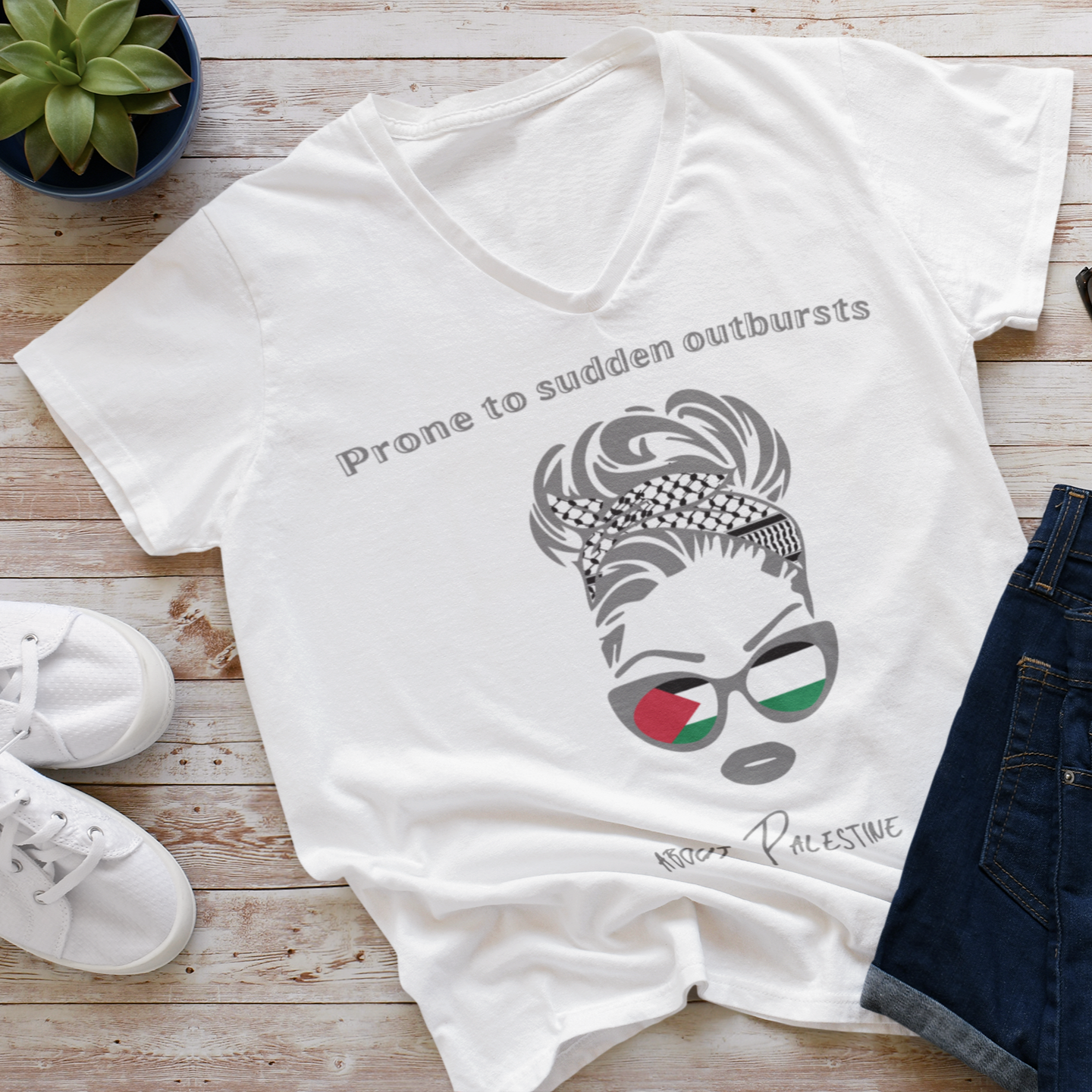 White t-shirt with graphic design and text on a wooden surface with shoes and sunglasses.