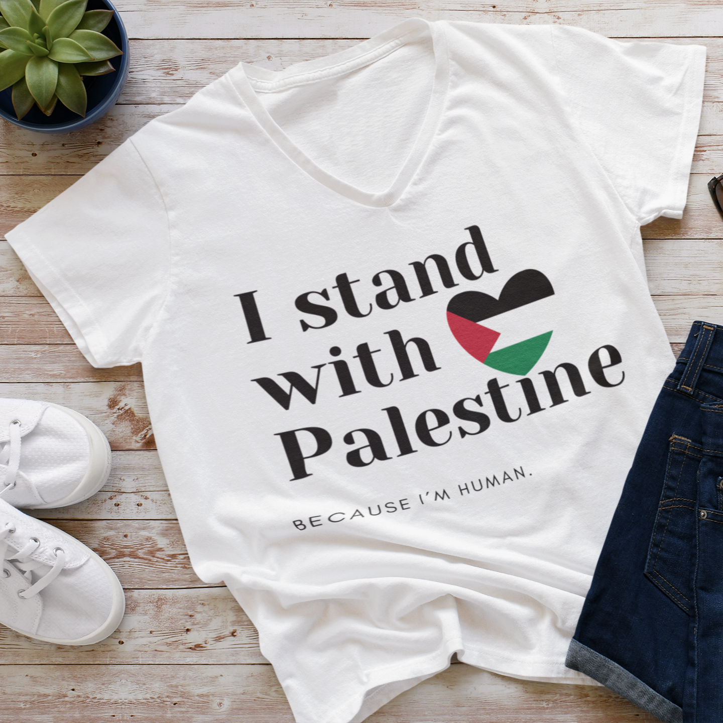 White t-shirt with 'I stand with Palestine' text on a wooden surface with shoes and sunglasses.