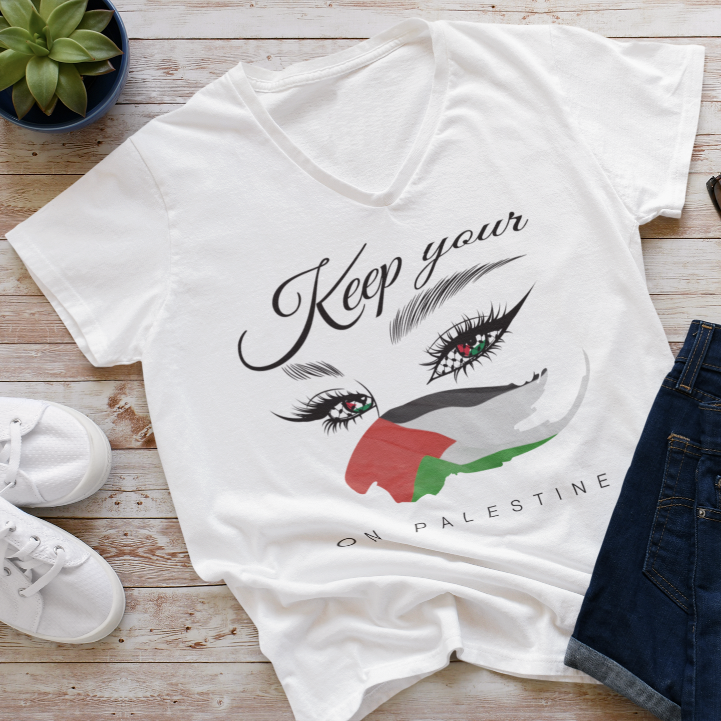 White t-shirt with graphic design and text on a wooden surface with shoes and jeans.