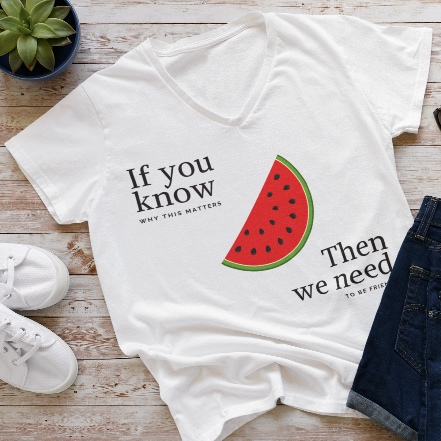 White t-shirt with watermelon graphic and text on a wooden surface with shoes and sunglasses.